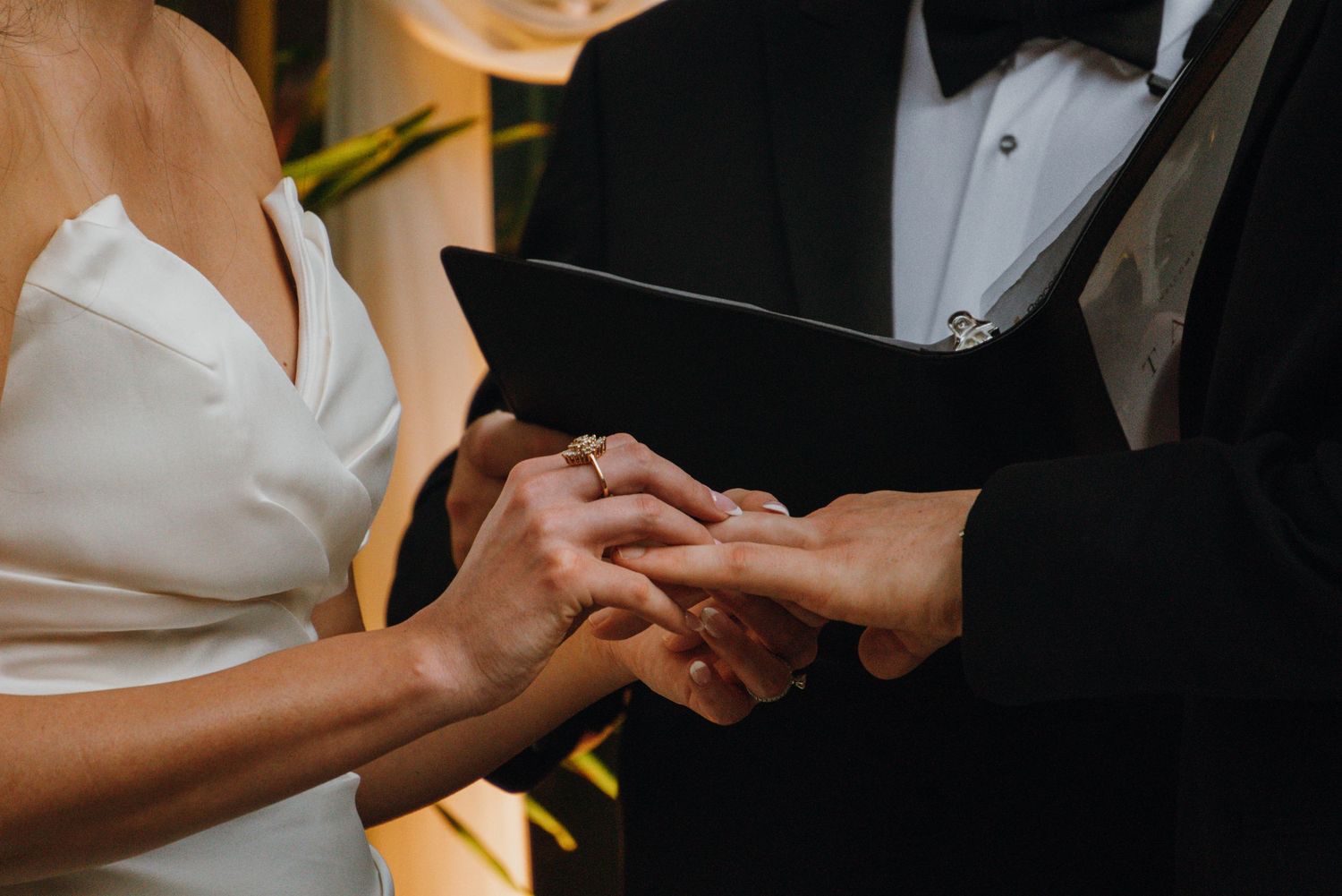 Close-up of bride and groom exchanging rings during wedding ceremony, bride in white gown.