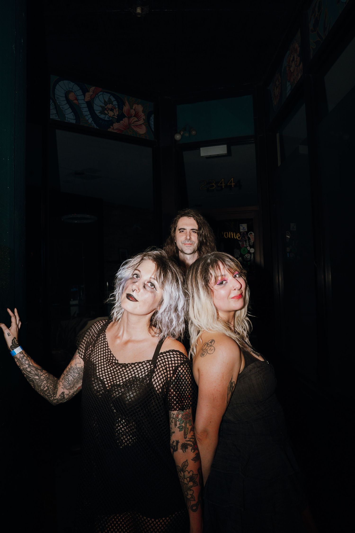 Three tattooed individuals posing together in a dark venue hallway after a concert.