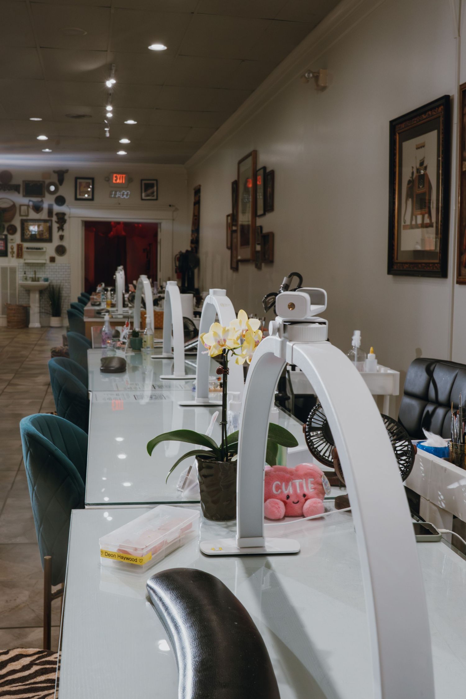 Modern nail salon interior with white manicure tables, teal chairs, and orchid centerpiece.