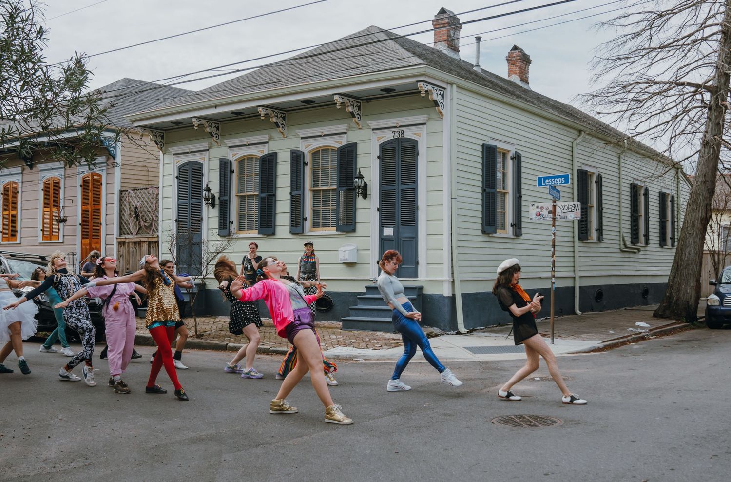 Group of dancers performing a second line parade on a New Orleans street past historic buildings.