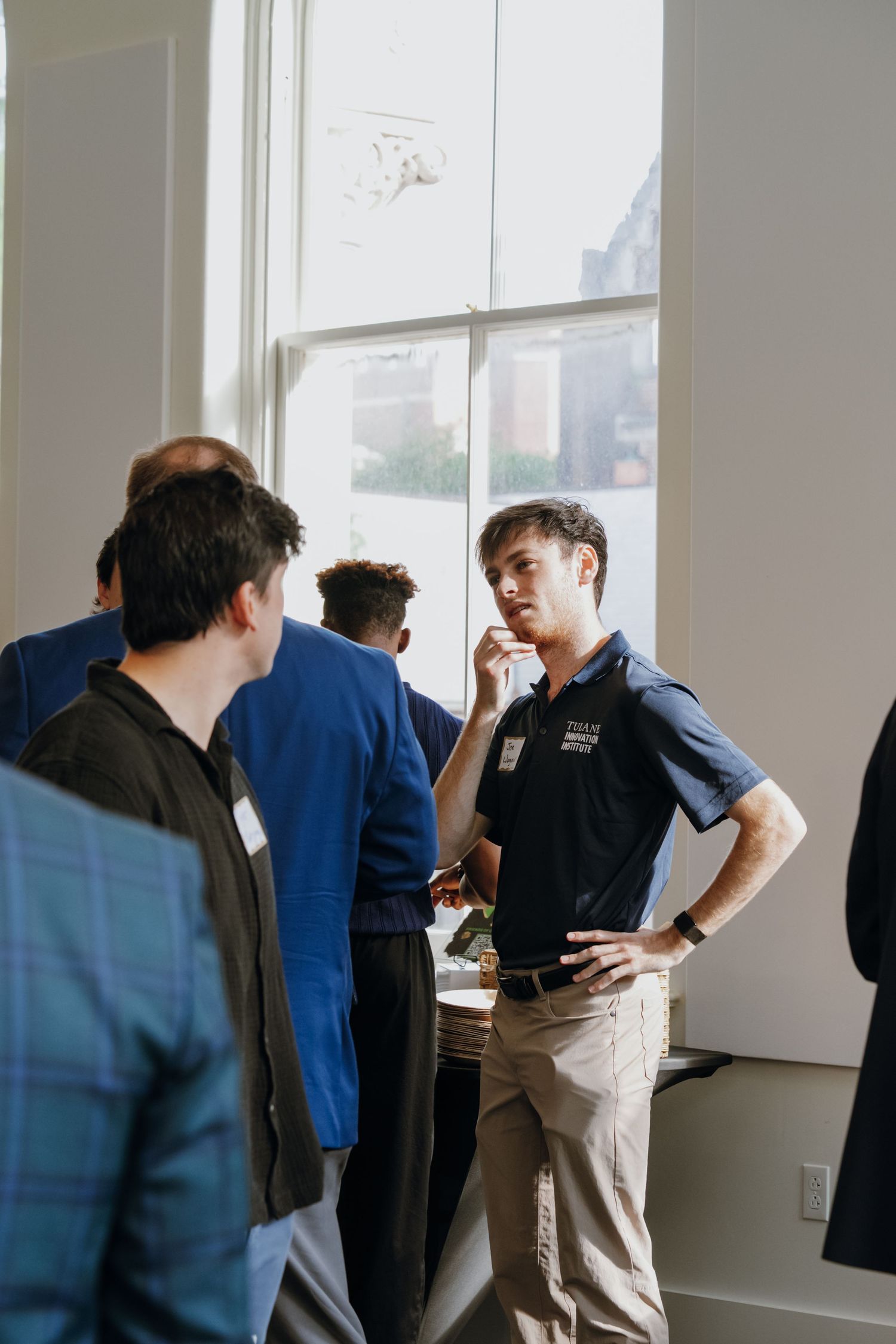 Young man in polo shirt converses with guests at indoor networking event.