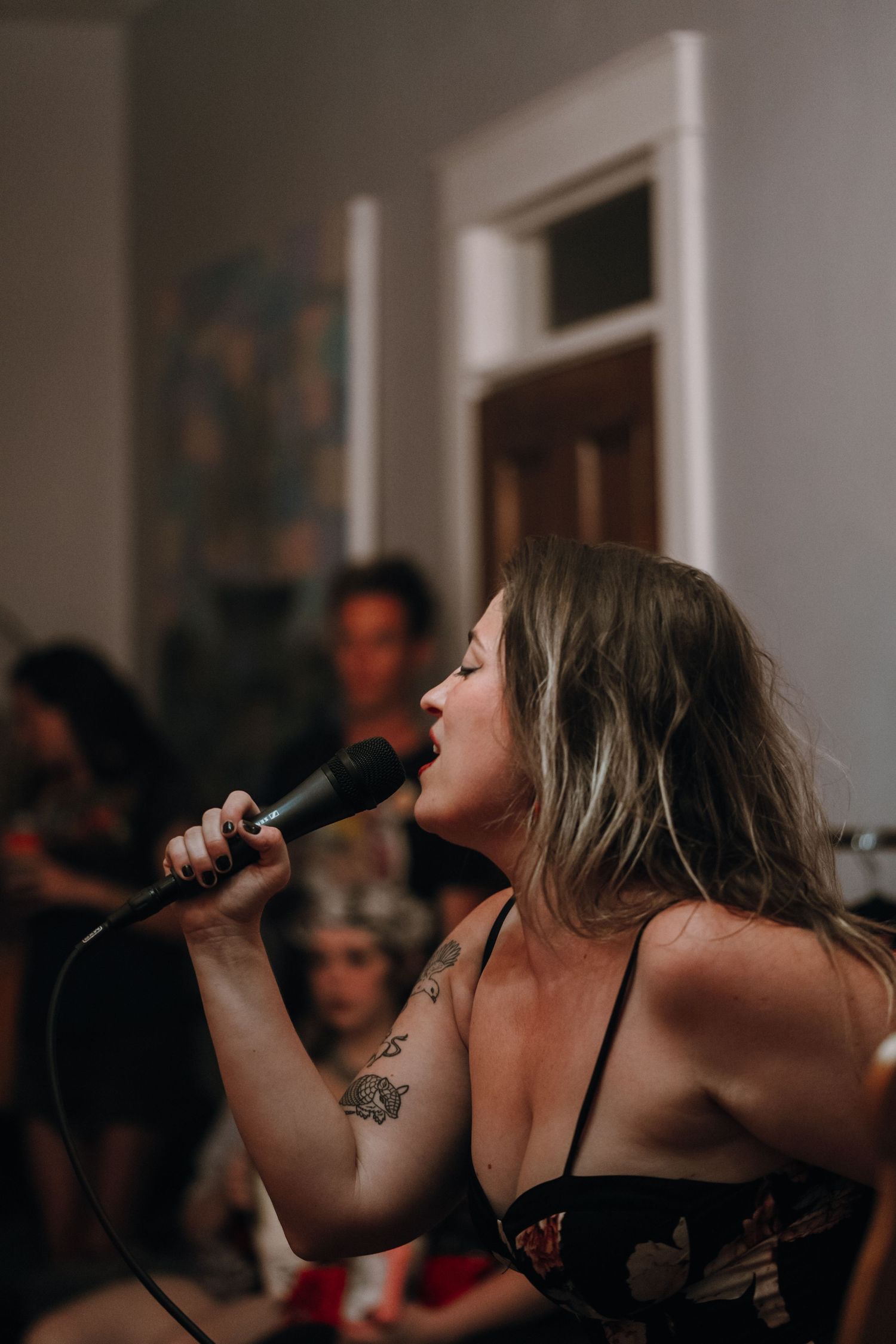 A tattooed woman singing passionately into a microphone at an indoor live music event.