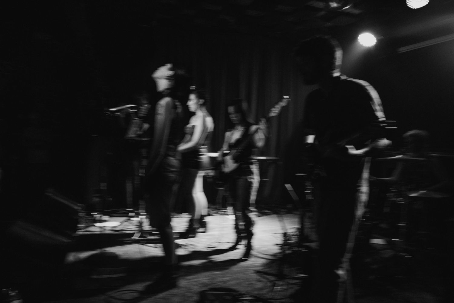Black and white blurred photo of band performing together on a dimly lit stage.