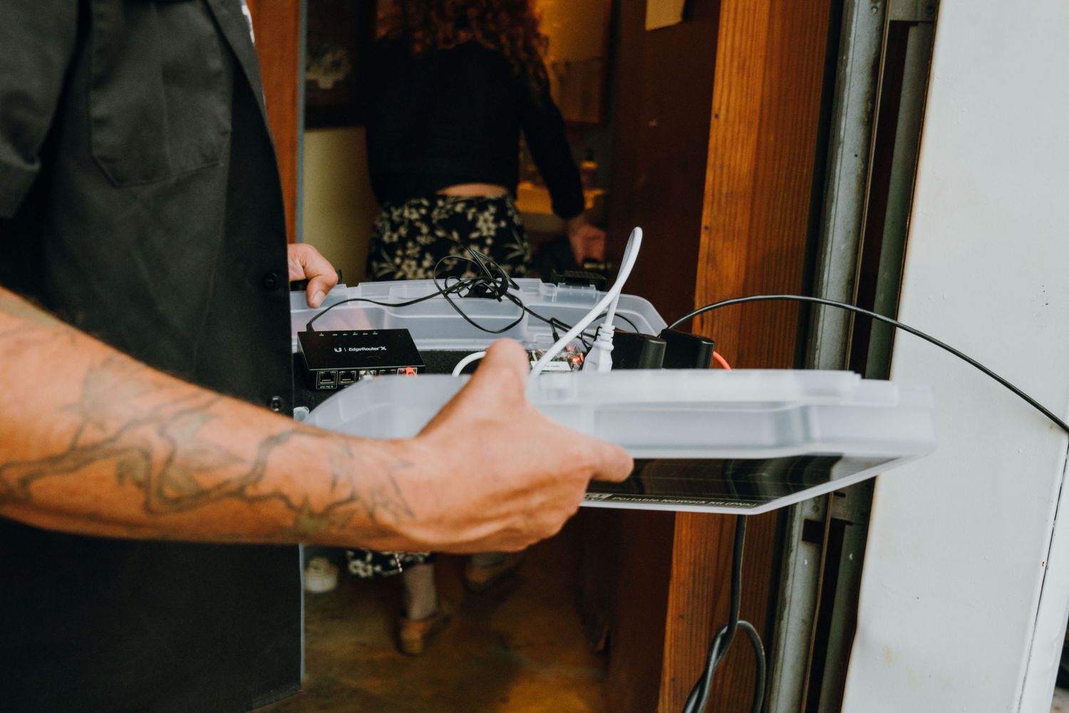 Tattooed arm holding a white darkroom developing tray with tongs in a photography lab.