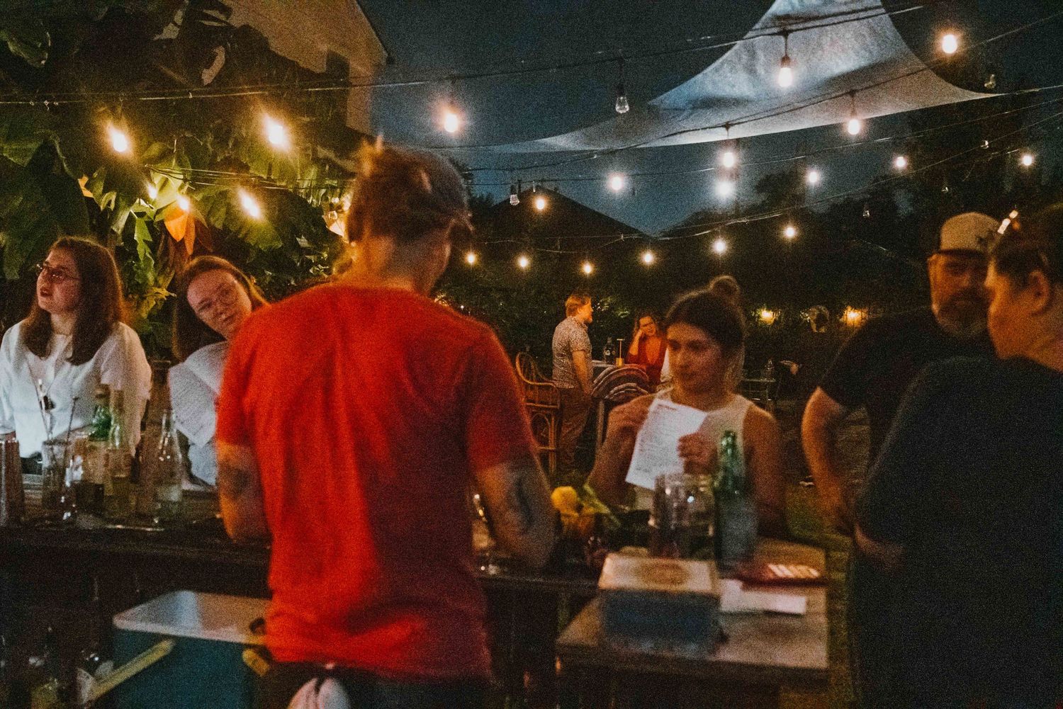 People socializing at an outdoor restaurant patio with warm string lights in the evening.