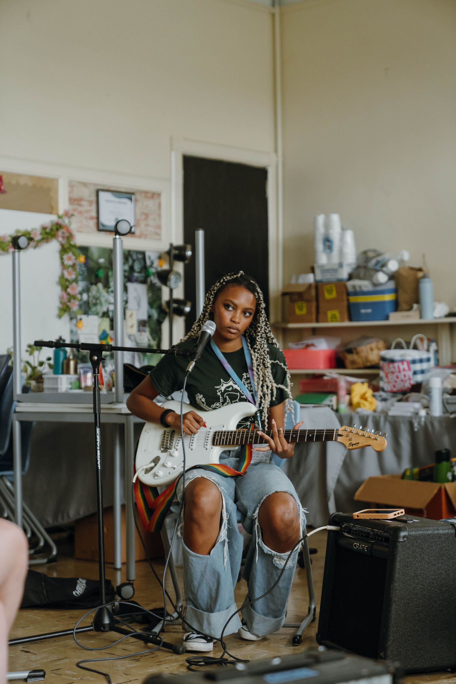 Young Black woman with braids plays white electric guitar seated before microphone in creative studio. New Orleans, Louisiana, Mississippi