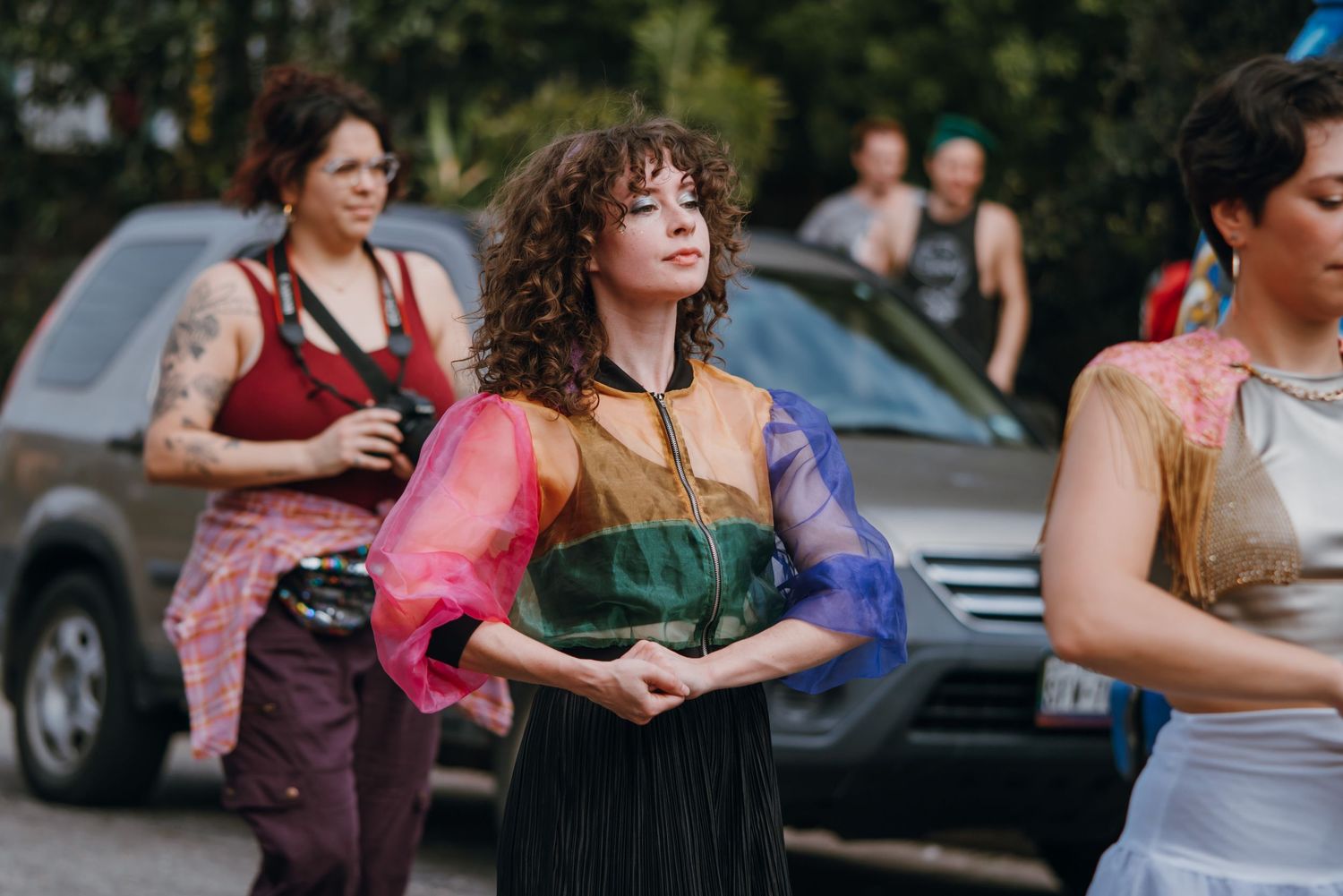 Woman in colorful sheer top dancing gracefully at an outdoor street performance event.