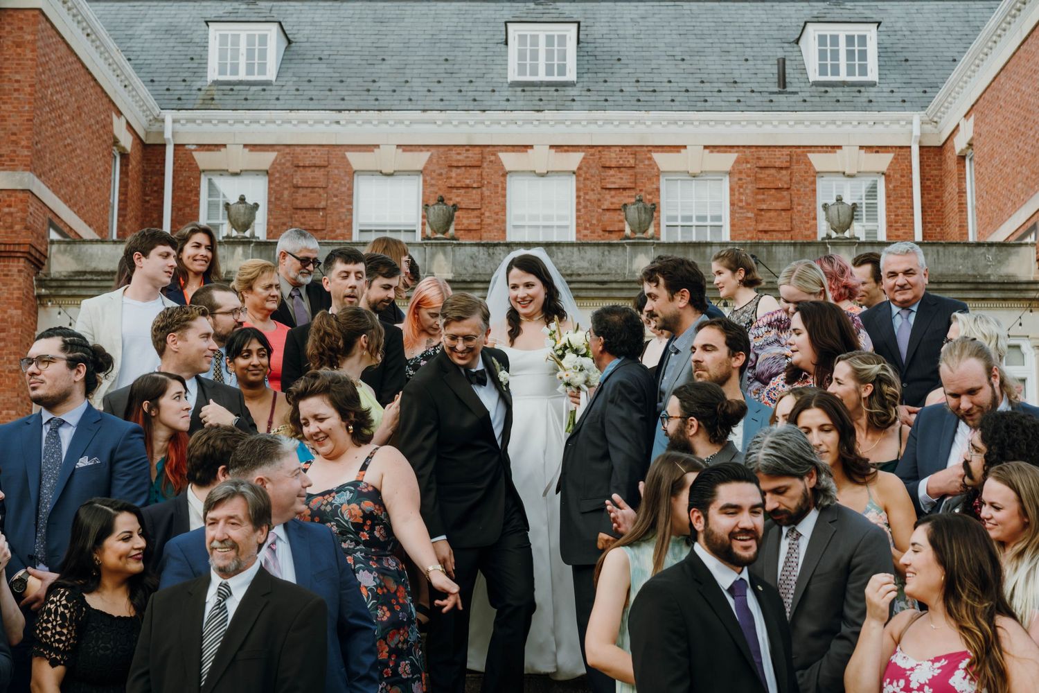 Large wedding party group photo on steps of a red brick venue with bride and groom at center. New Orleans, Louisiana, Mississippi