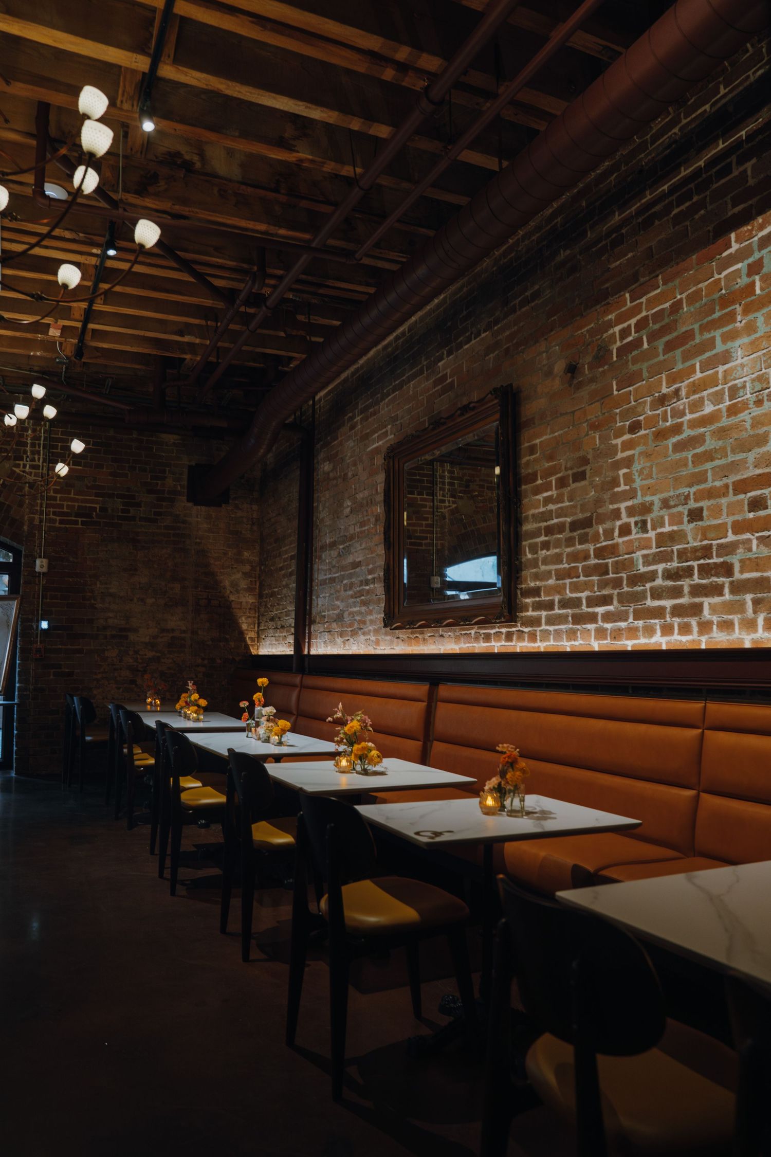 Dimly lit restaurant interior with brick walls, leather booths, wooden tables, and globe pendant lights.