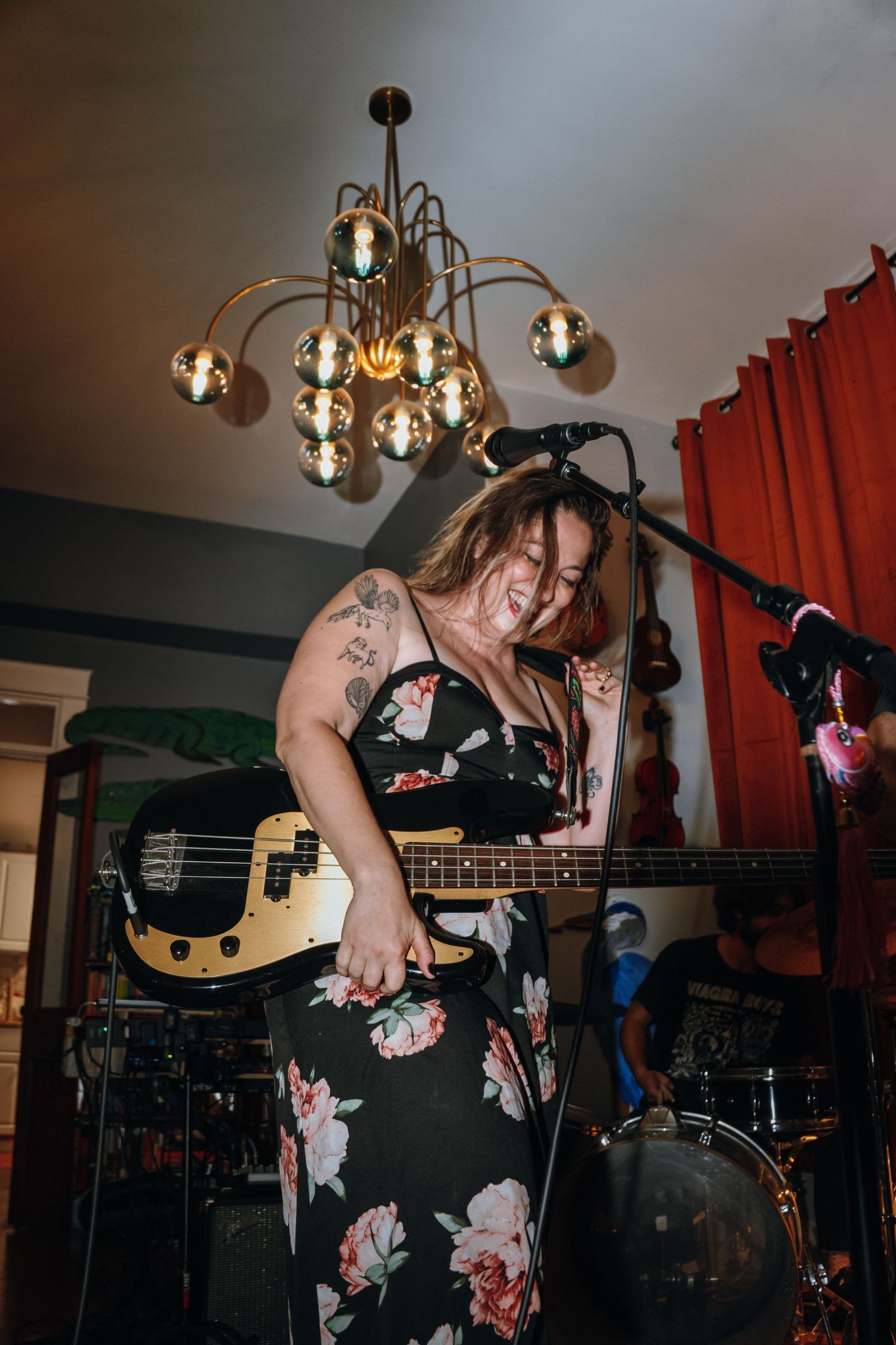 Woman in floral dress playing electric guitar under gold chandelier at indoor music performance.
