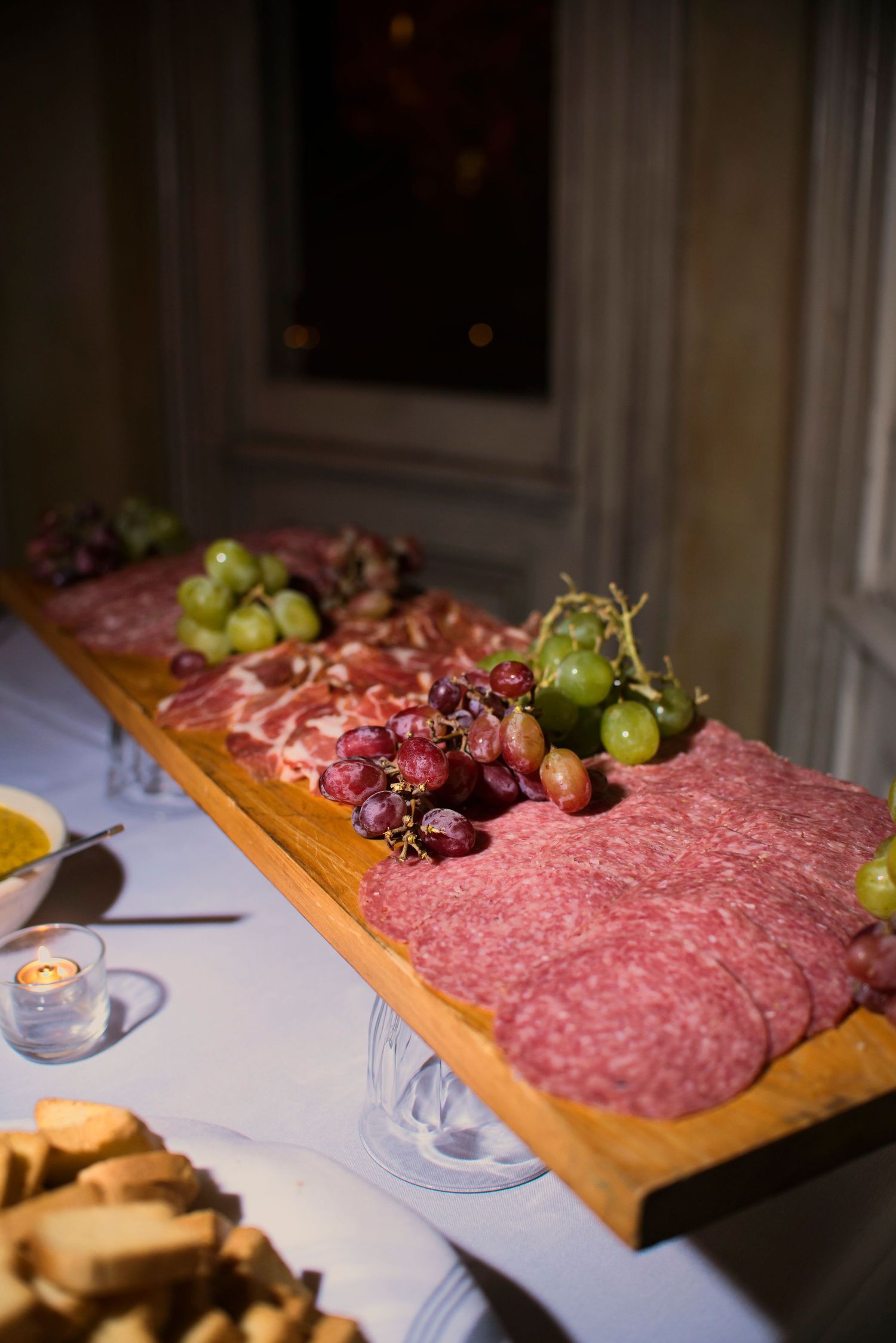 Elegant charcuterie board with sliced salami, red and green grapes arranged on a wooden platter at a catered event.