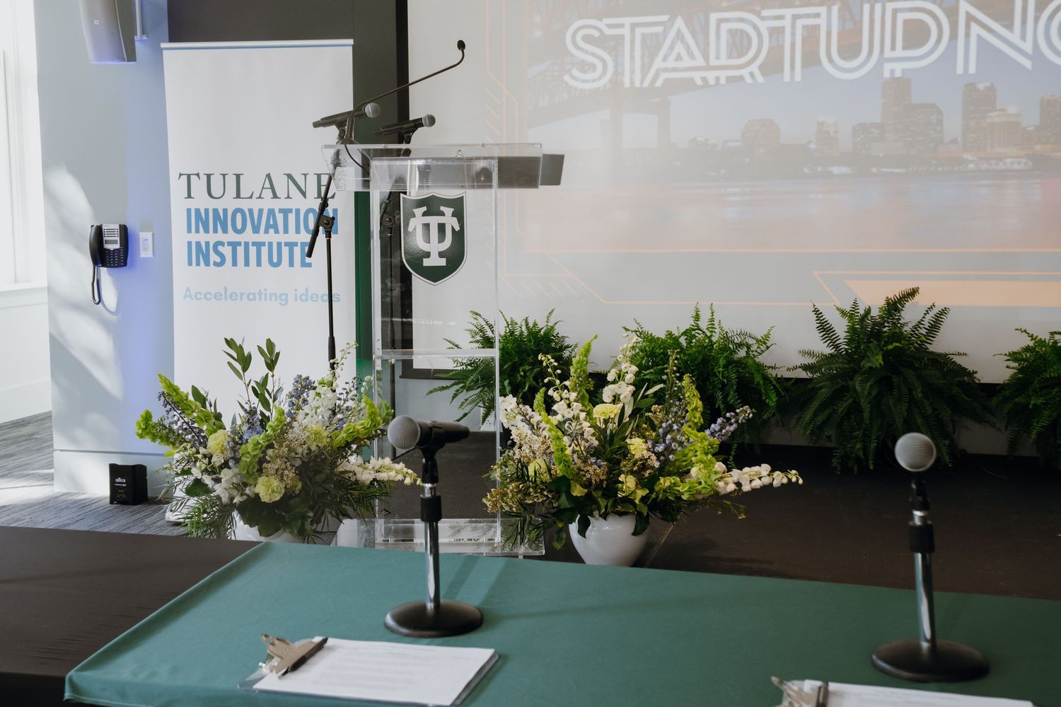 Tulane Innovation Institute startup event stage with floral arrangements, podium, and microphones in an elegant conference setting.