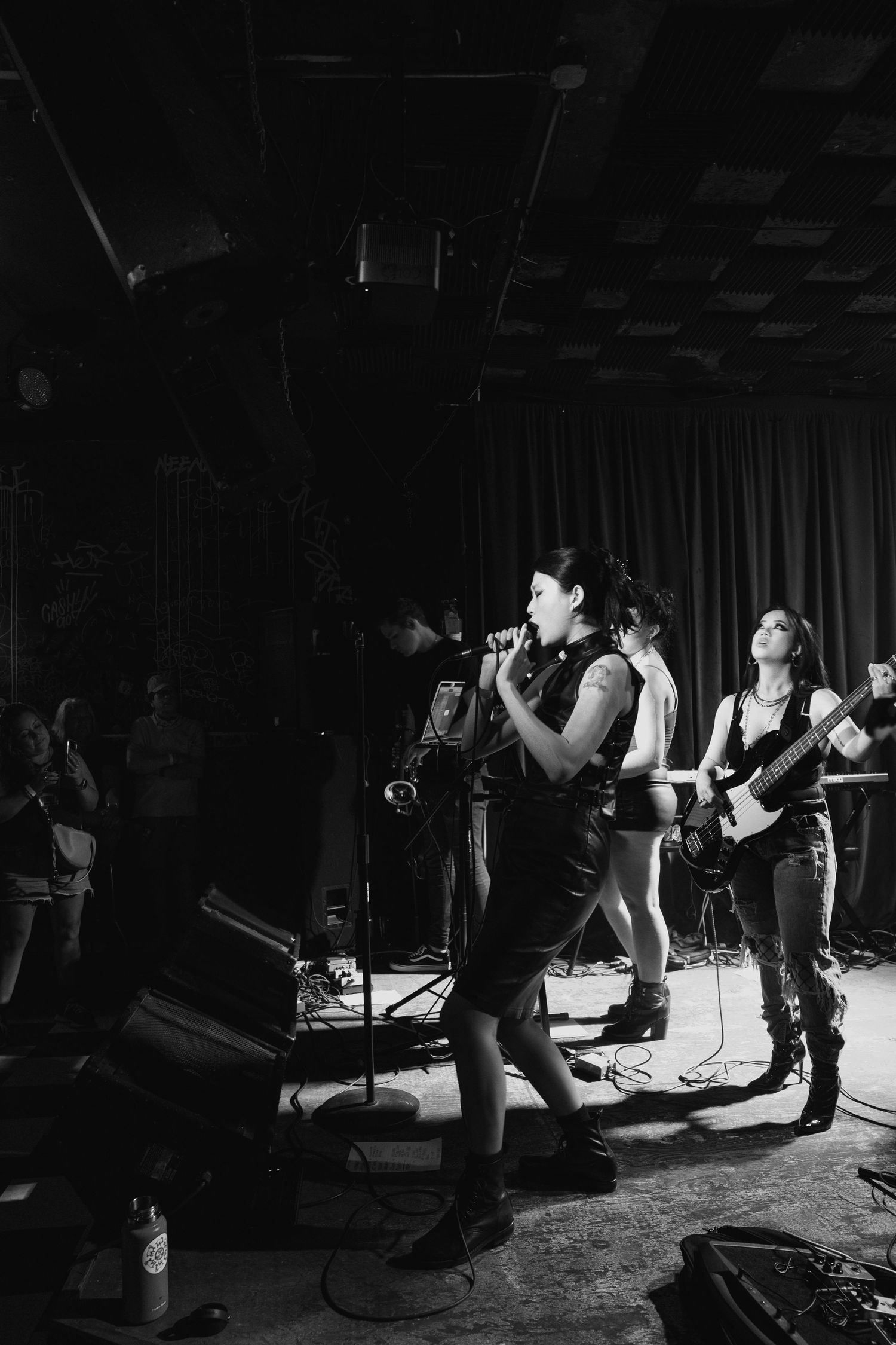 Black and white photo of female vocalist and bassist performing on stage for live audience.