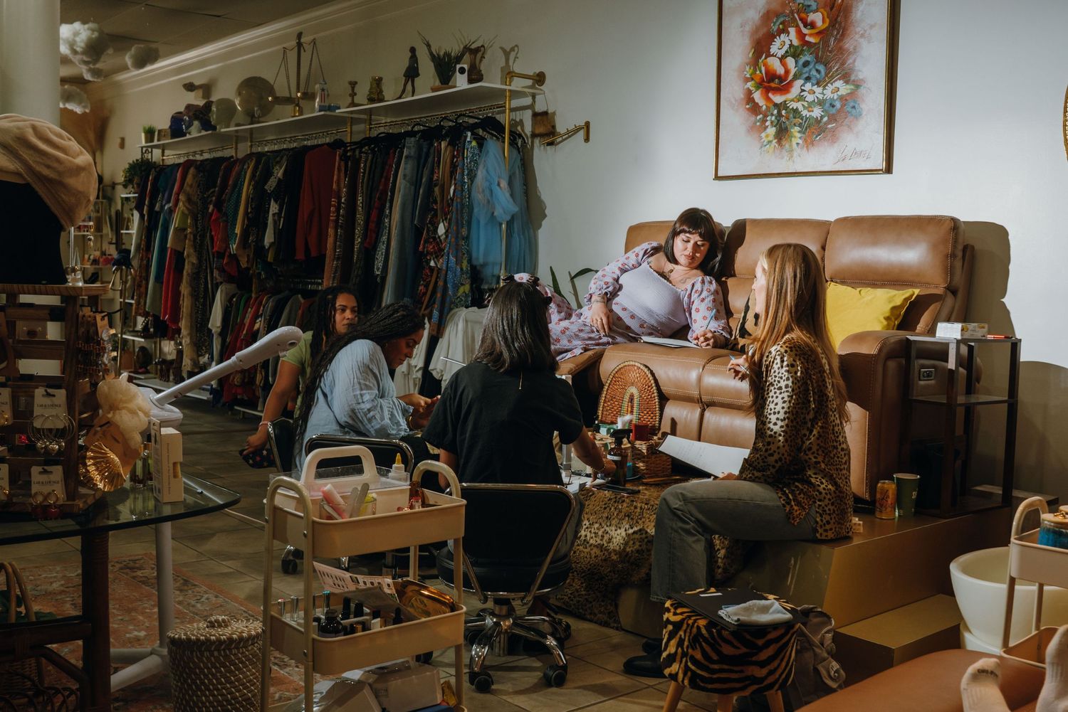 Women socializing in a vintage nail salon lounge with clothing racks and retro decor in New Orleans.