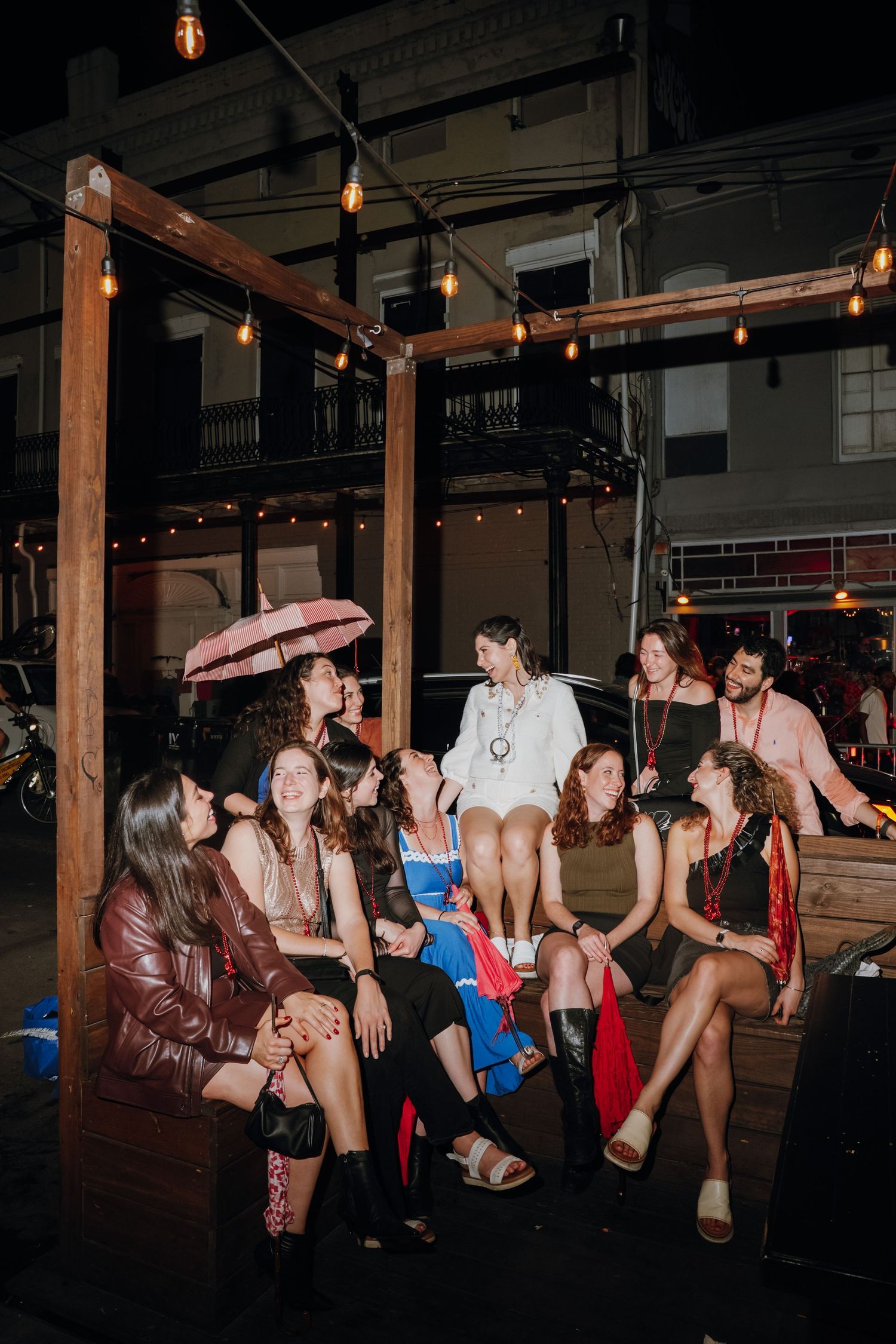Group of women gathered at night under string lights on a wooden structure at an outdoor party.