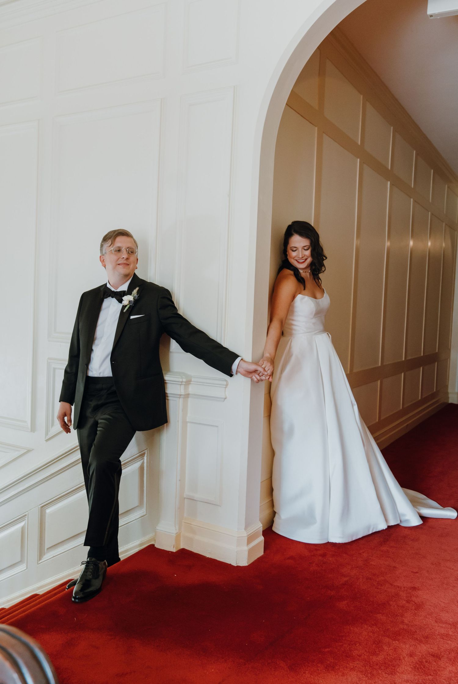 Bride and groom holding hands around a white archway on a red carpeted staircase before their first look. New Orleans, Louisiana, Mississipp