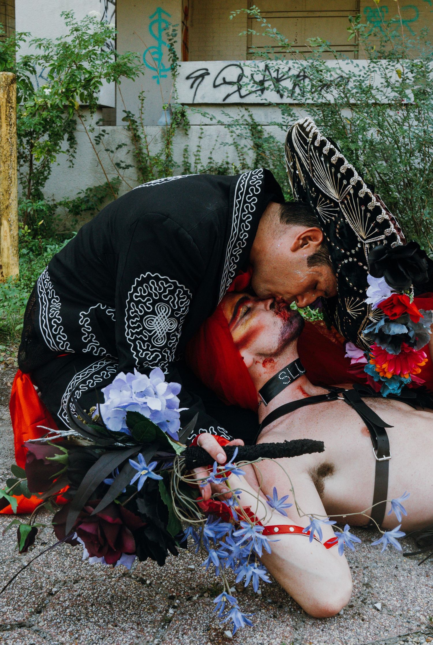 Person in mariachi hat leaning over a flower-adorned figure lying on the ground.