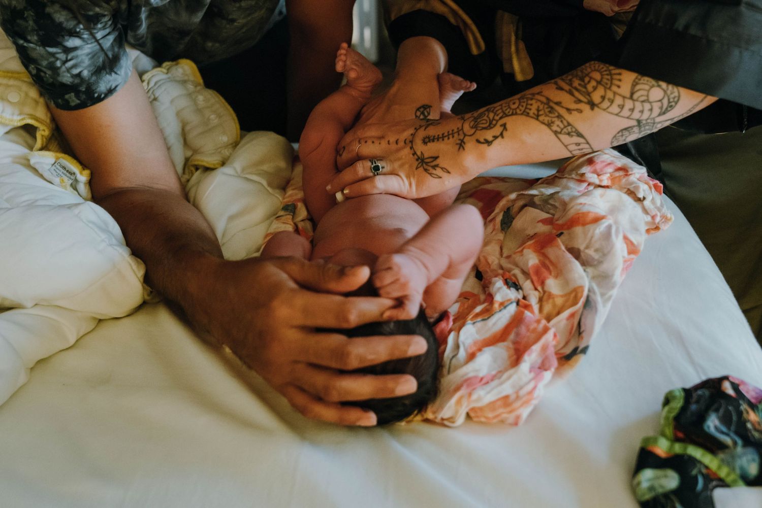 Close-up of multiple hands lovingly cradling newborn baby wrapped in colorful floral blanket. New Orleans, Louisiana, Mississippi
