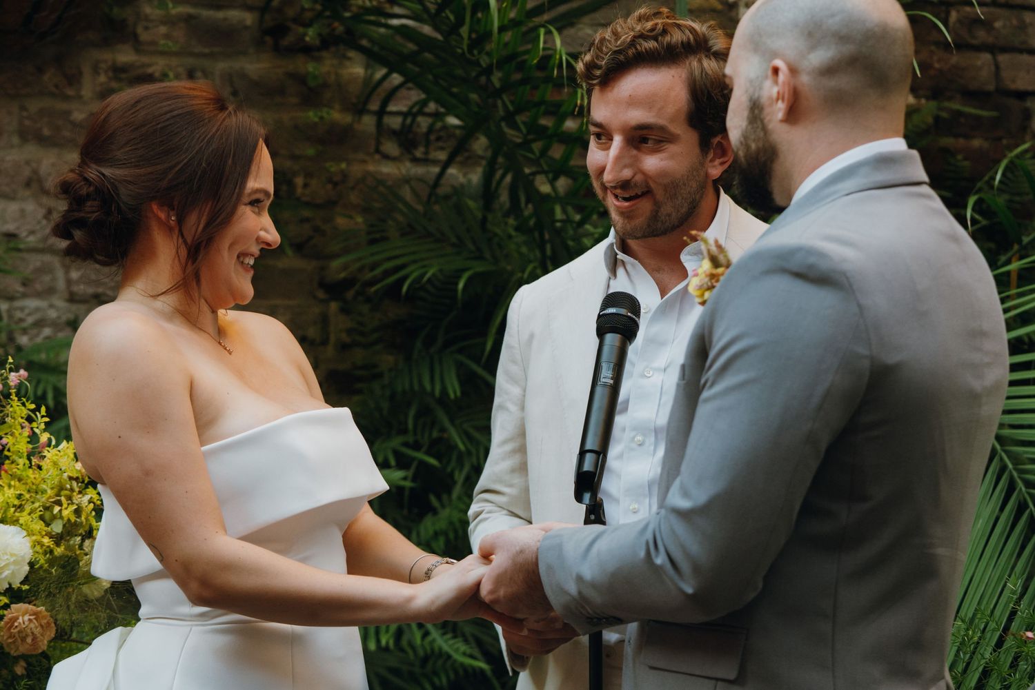 Bride and groom hold hands smiling during intimate outdoor wedding ceremony officiated by man in white suit. New Orleans, Louisiana, Mississ