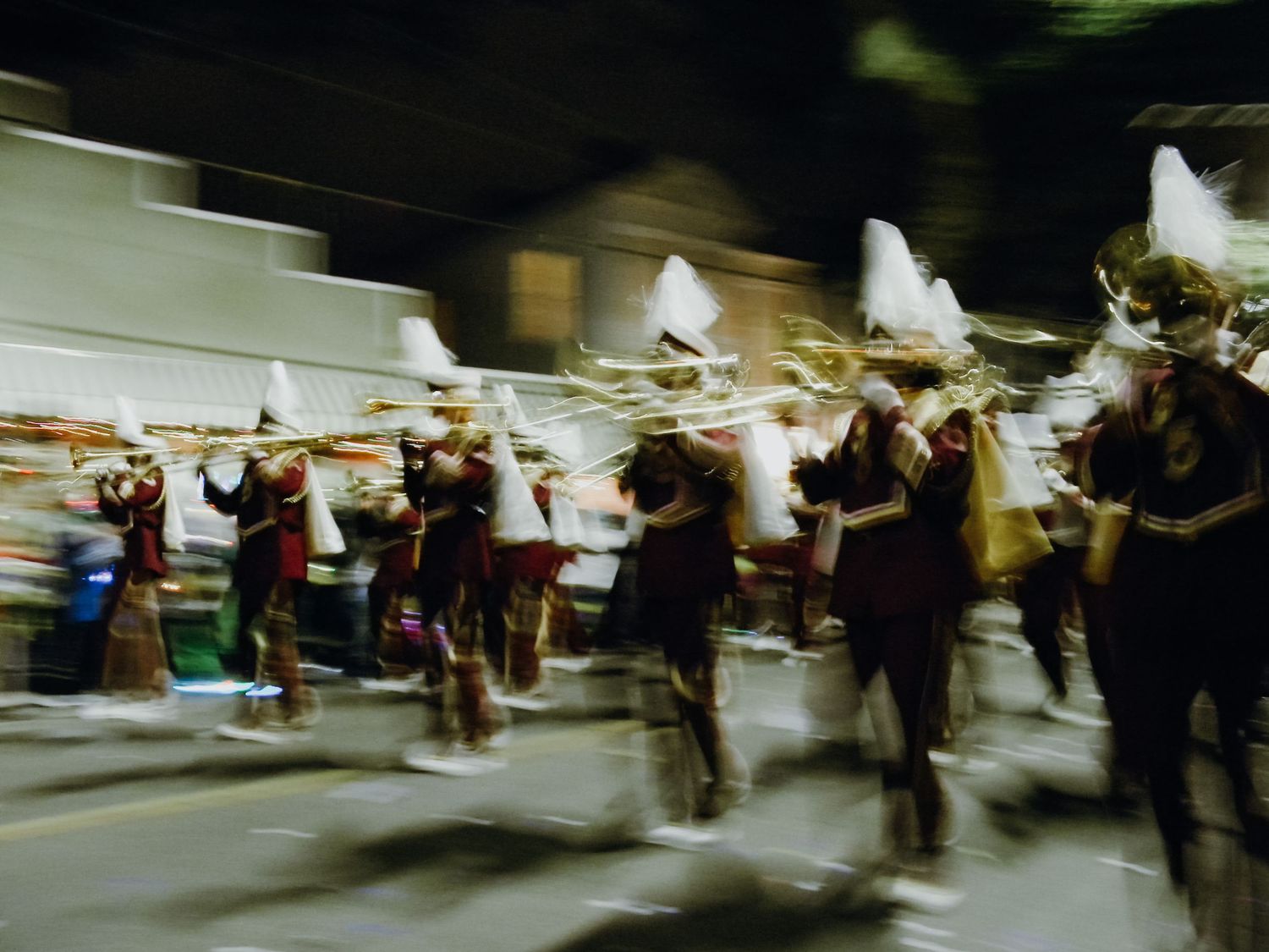 A blurred motion shot of a marching band performing at a nighttime parade.