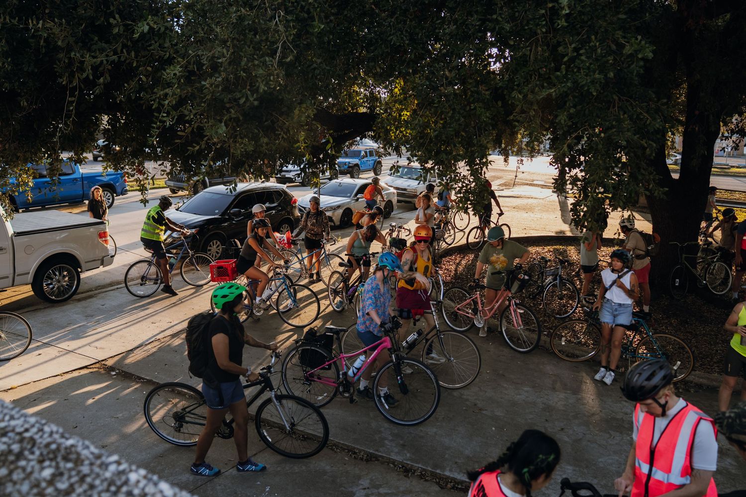 Large group of cyclists gathering under trees at outdoor community bike ride event.