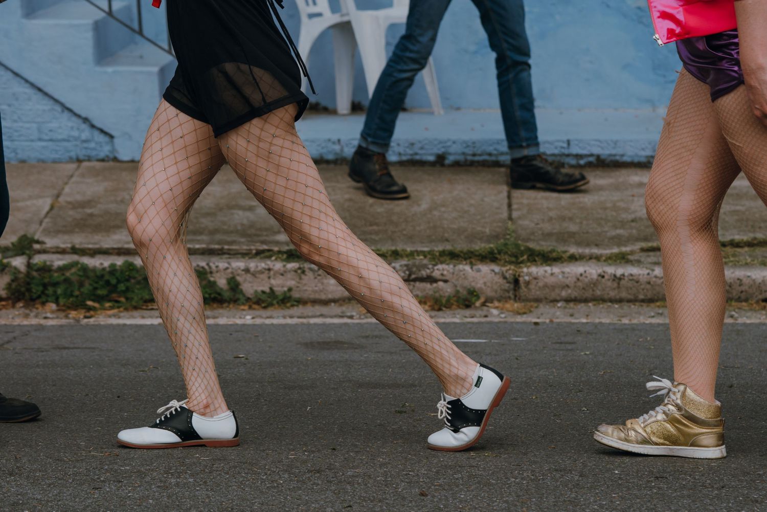 Close-up of dancers' legs in fishnet stockings and saddle shoes on a street.