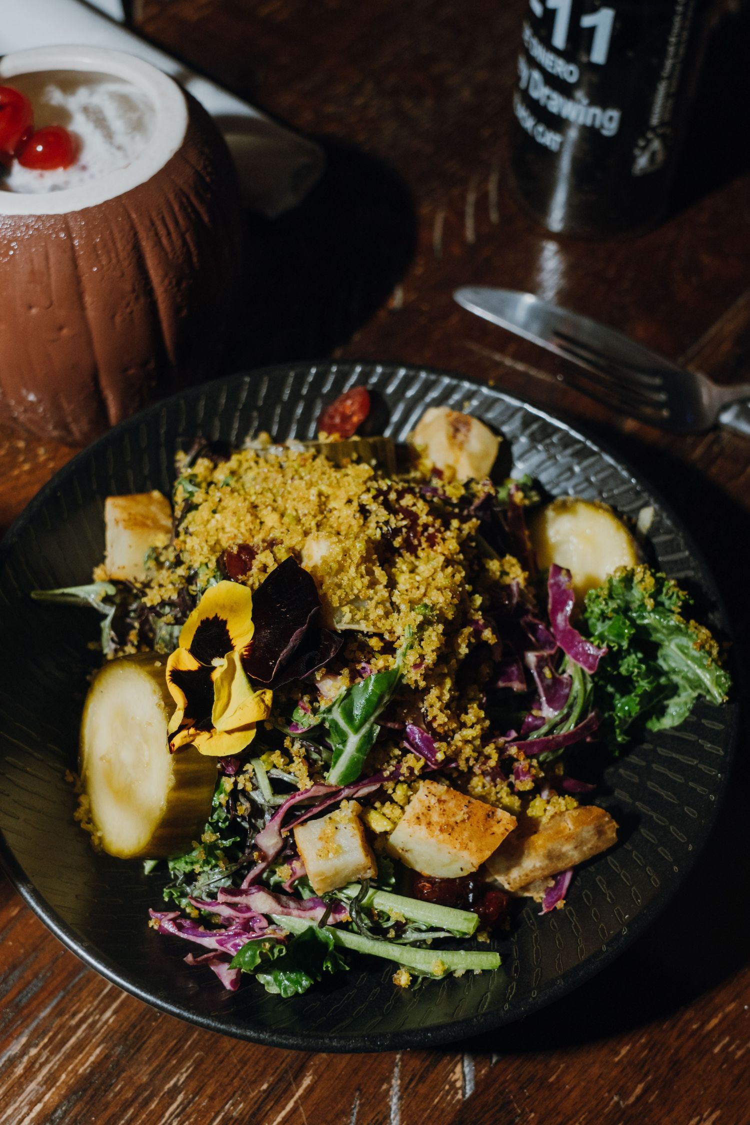 Colorful quinoa salad with seared chicken, purple cabbage, kale, and edible flowers on a dark plate.