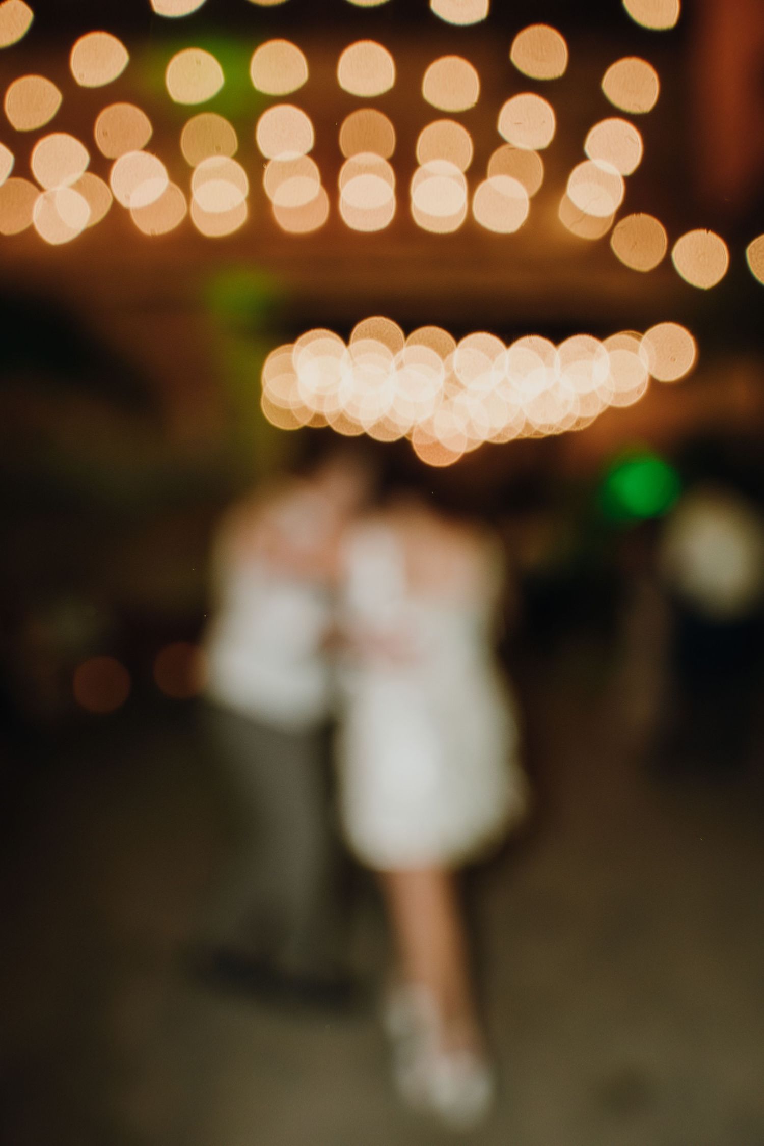 Blurred couple sharing first dance under warm bokeh string lights at wedding reception. New Orleans, Louisiana, Mississippi