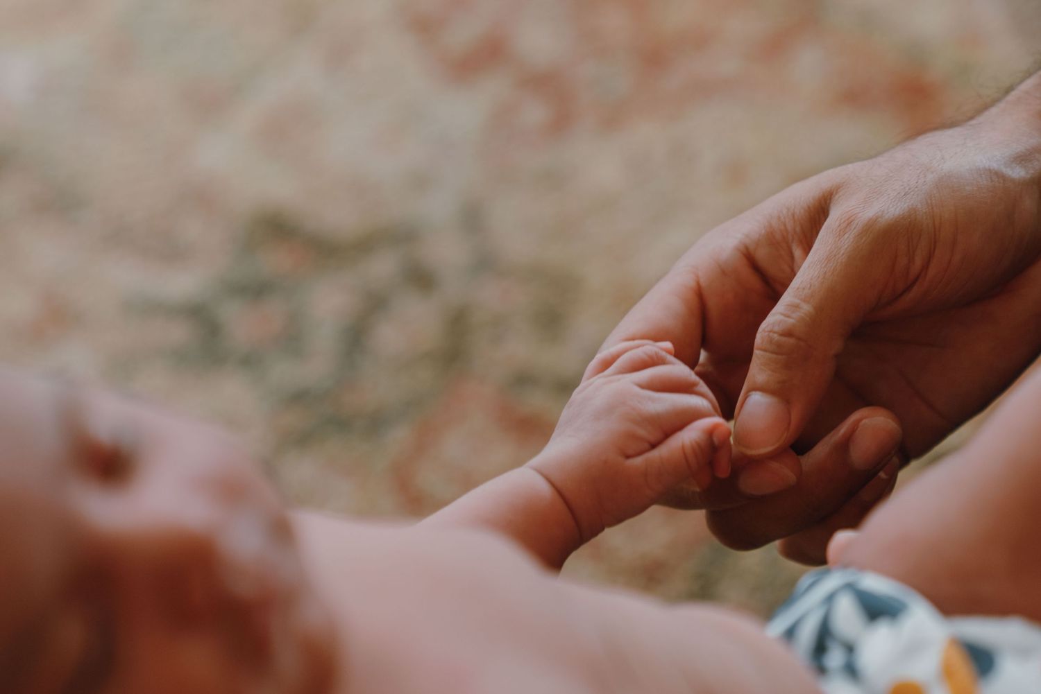 Tender moment of adult fingers gently holding tiny newborn baby hand on patterned rug. New Orleans, Louisiana, Mississippi