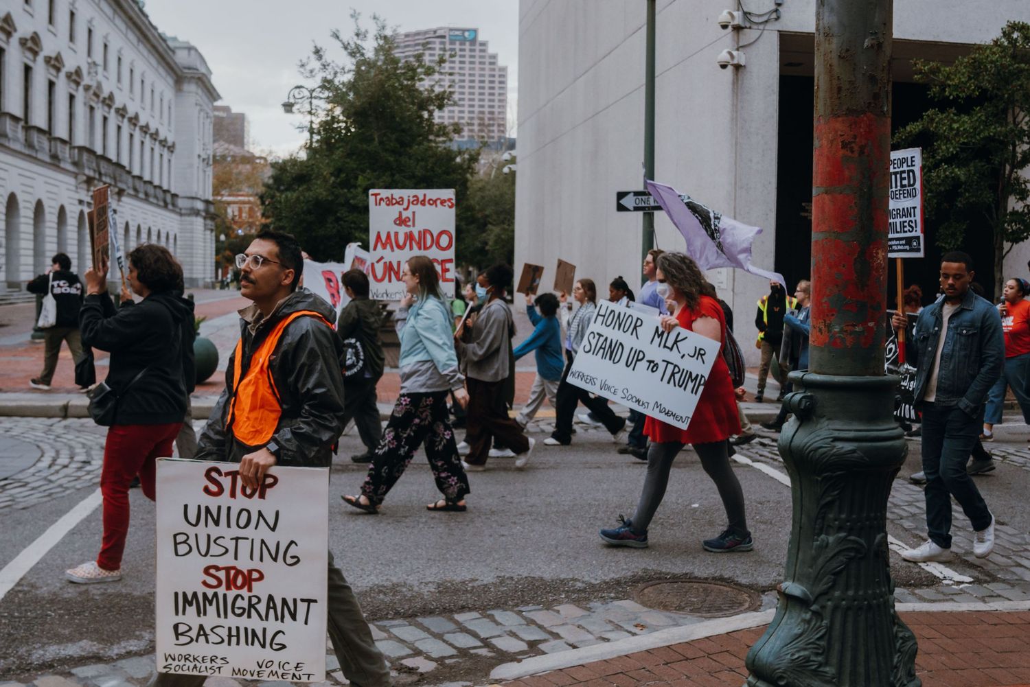Protesters march past a government building holding signs about union busting and immigrant rights.