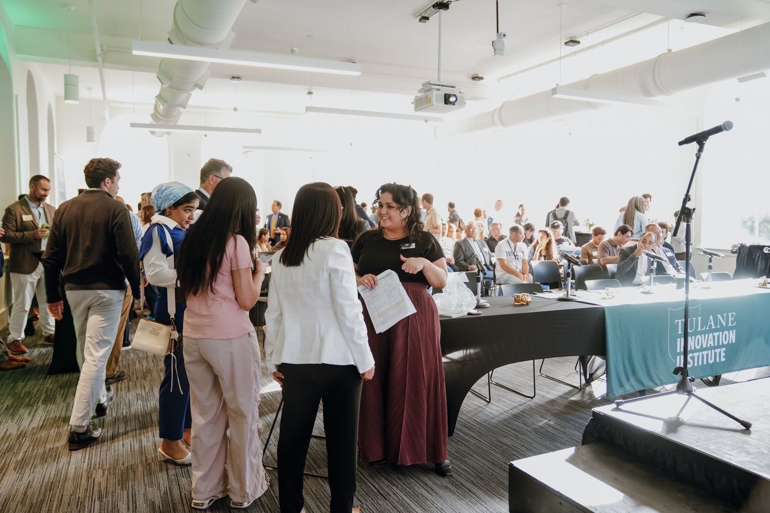 Diverse group of attendees mingling at Tulane Innovation Institute conference in bright modern venue.