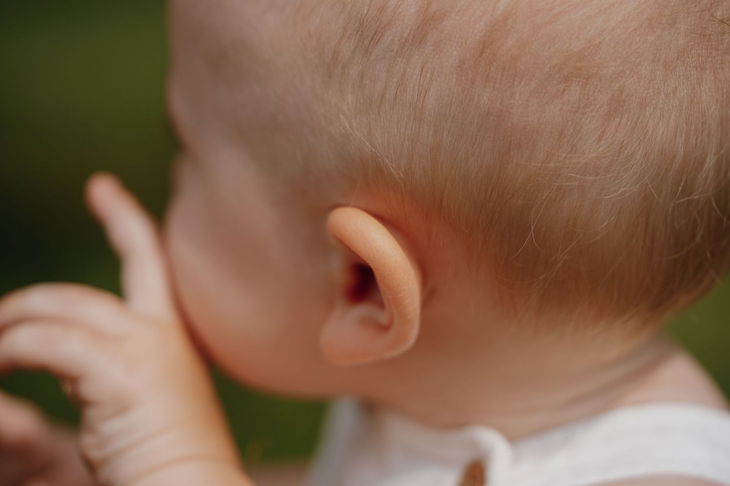 Close-up of a baby's ear and profile with soft focus green background.
