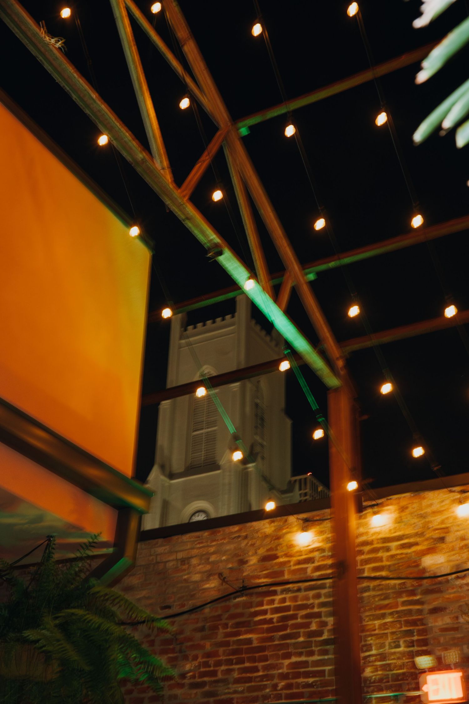 Low angle view of string lights and bamboo structure at outdoor wedding venue with brick wall and church tower. New Orleans, Louisiana, Miss