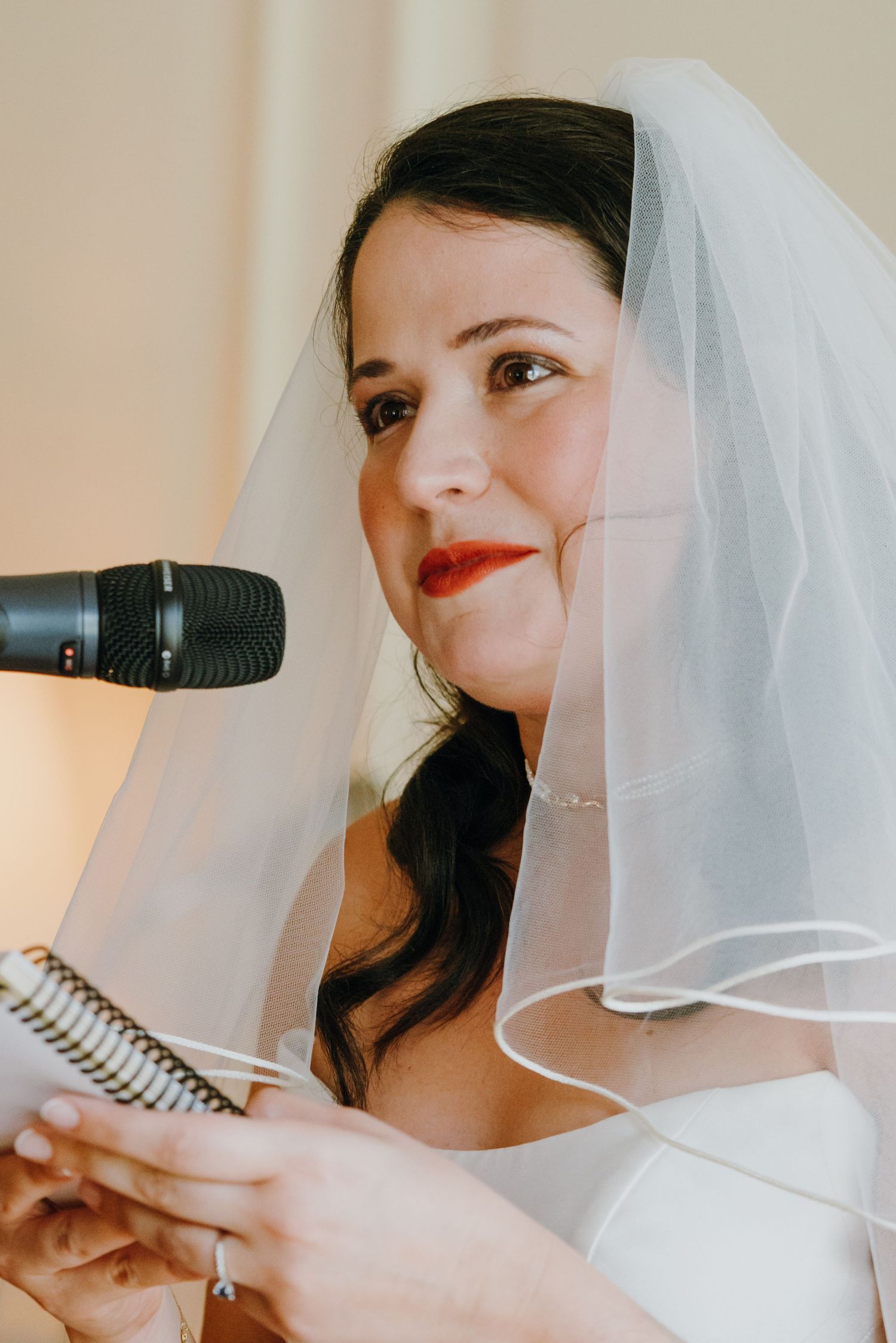 Beautiful bride in white veil with red lips reading vows at microphone during ceremony. New Orleans, Louisiana, Mississippi