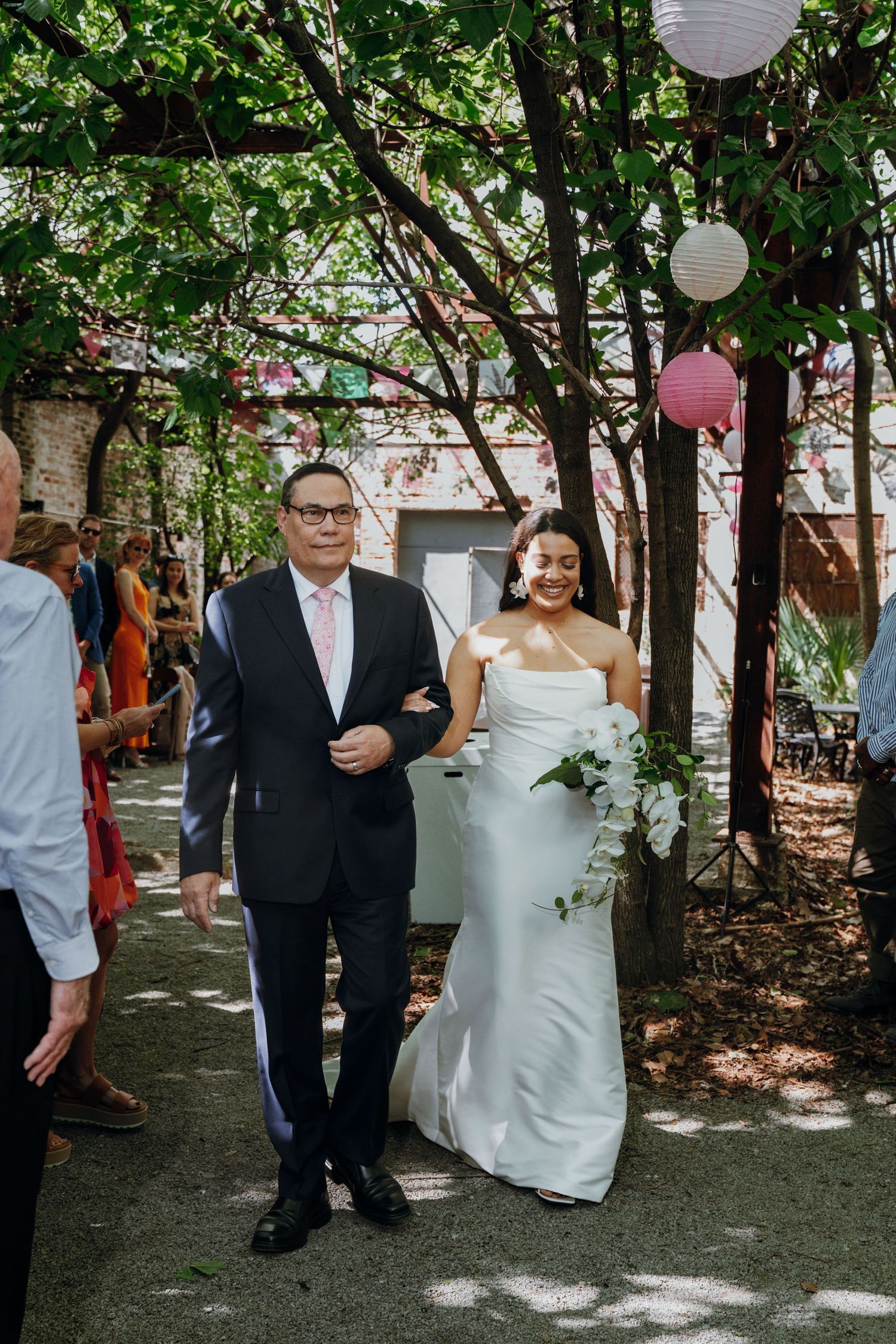 Bride in a white gown walking down the aisle with her father at an outdoor wedding.