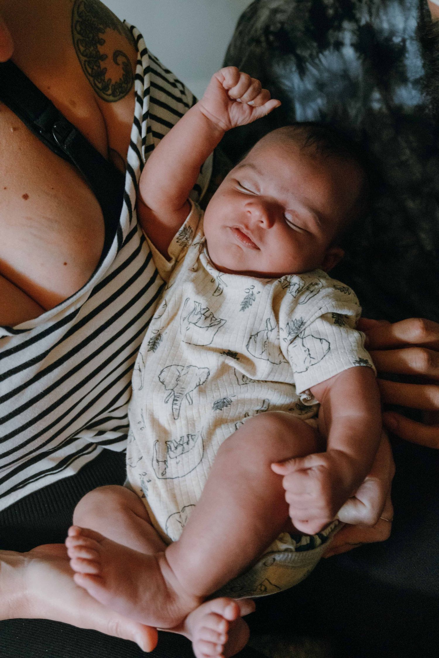 Peaceful newborn baby in floral onesie resting in mothers tattooed arms with fist raised. New Orleans, Louisiana, Mississippi