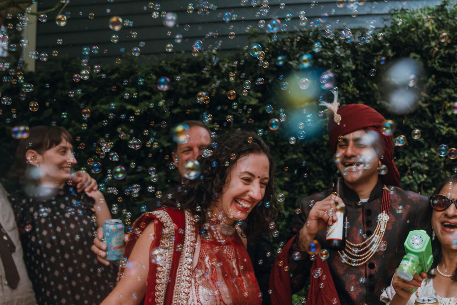 Bride and groom laughing joyfully surrounded by floating bubbles at Indian wedding celebration.