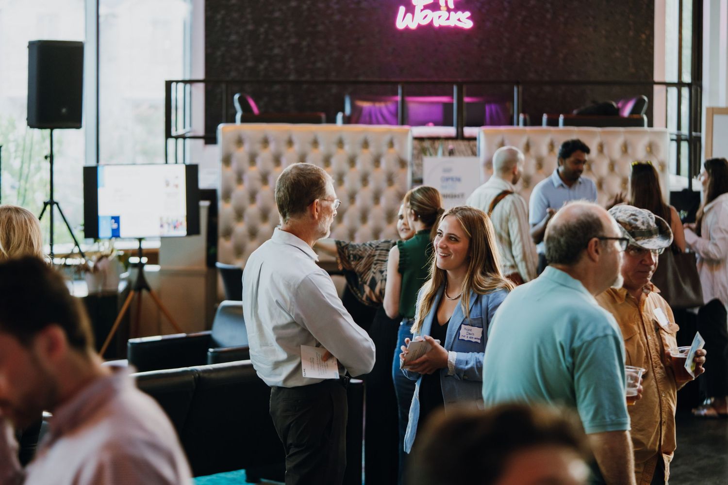Professionals networking at a corporate event in a modern venue with neon signs and elegant decor.