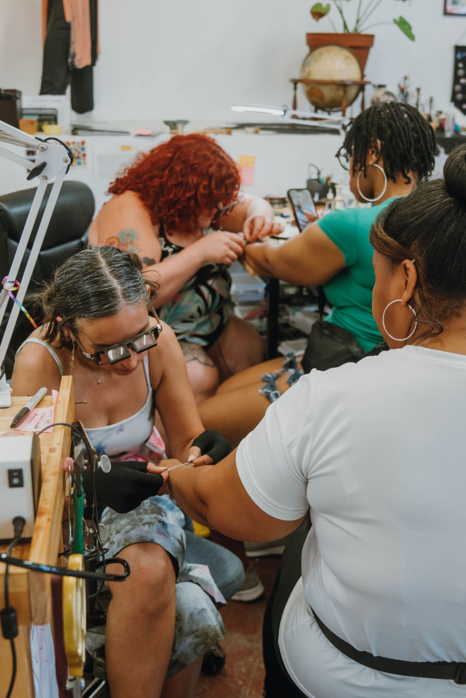 Tattoo artist giving a tattoo to a client in a busy, eclectic tattoo studio with multiple people.