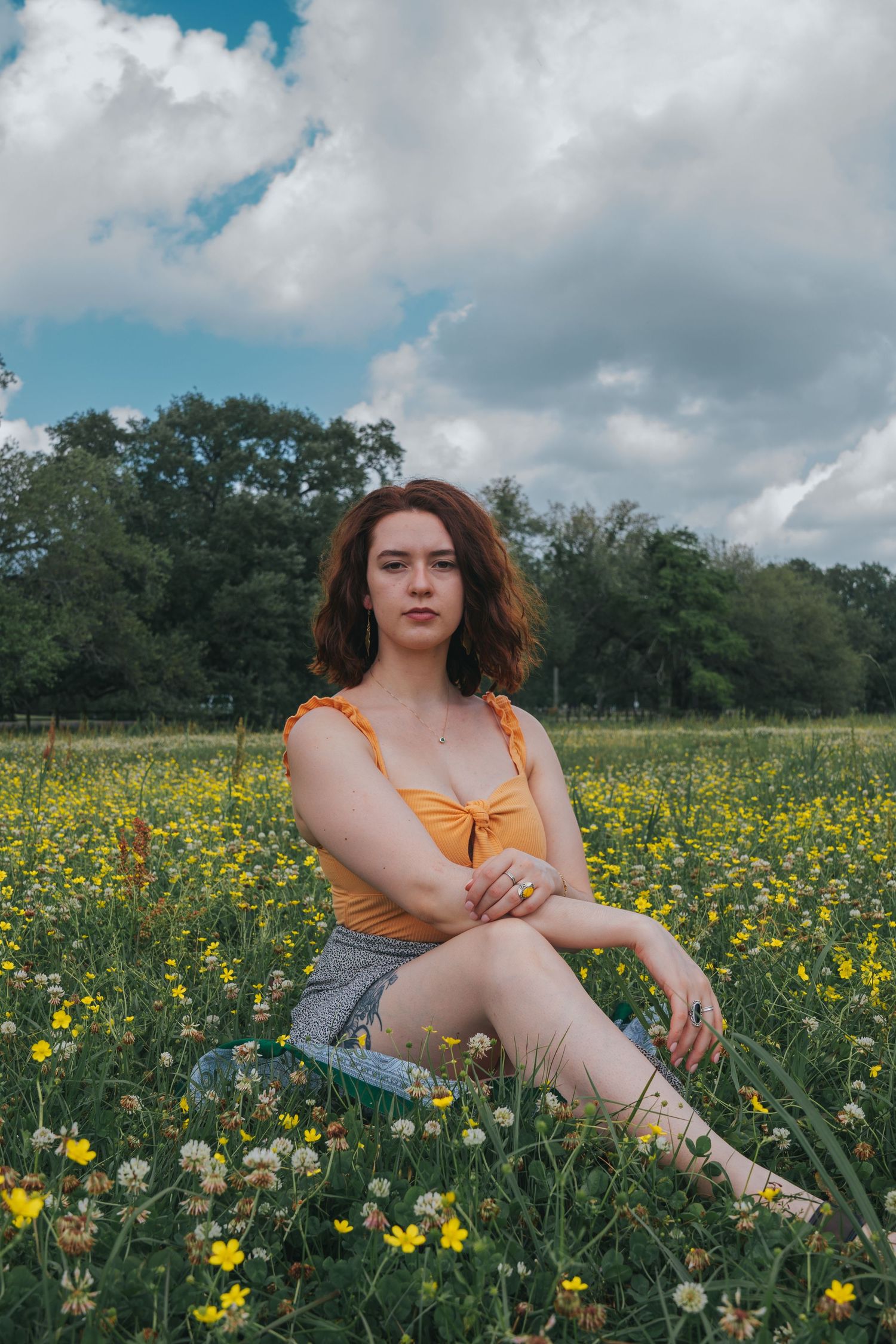 Young woman in yellow top and gray shorts sitting gracefully in a vibrant wildflower meadow.