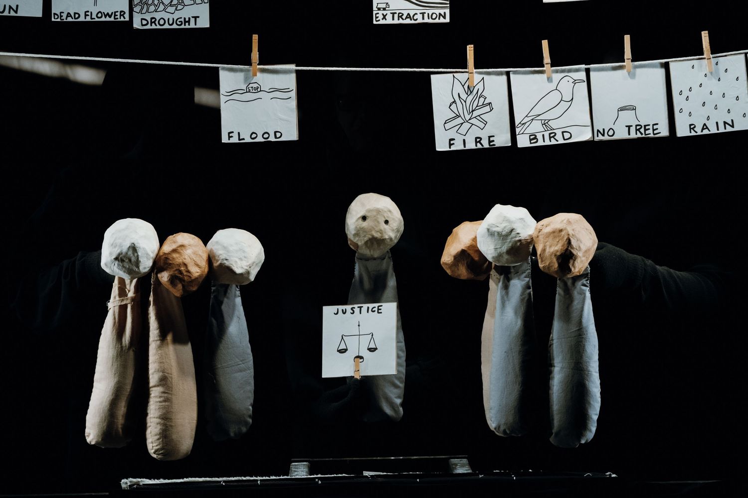 Three puppet figures with round heads holding signs under hanging illustrated word cards on stage.