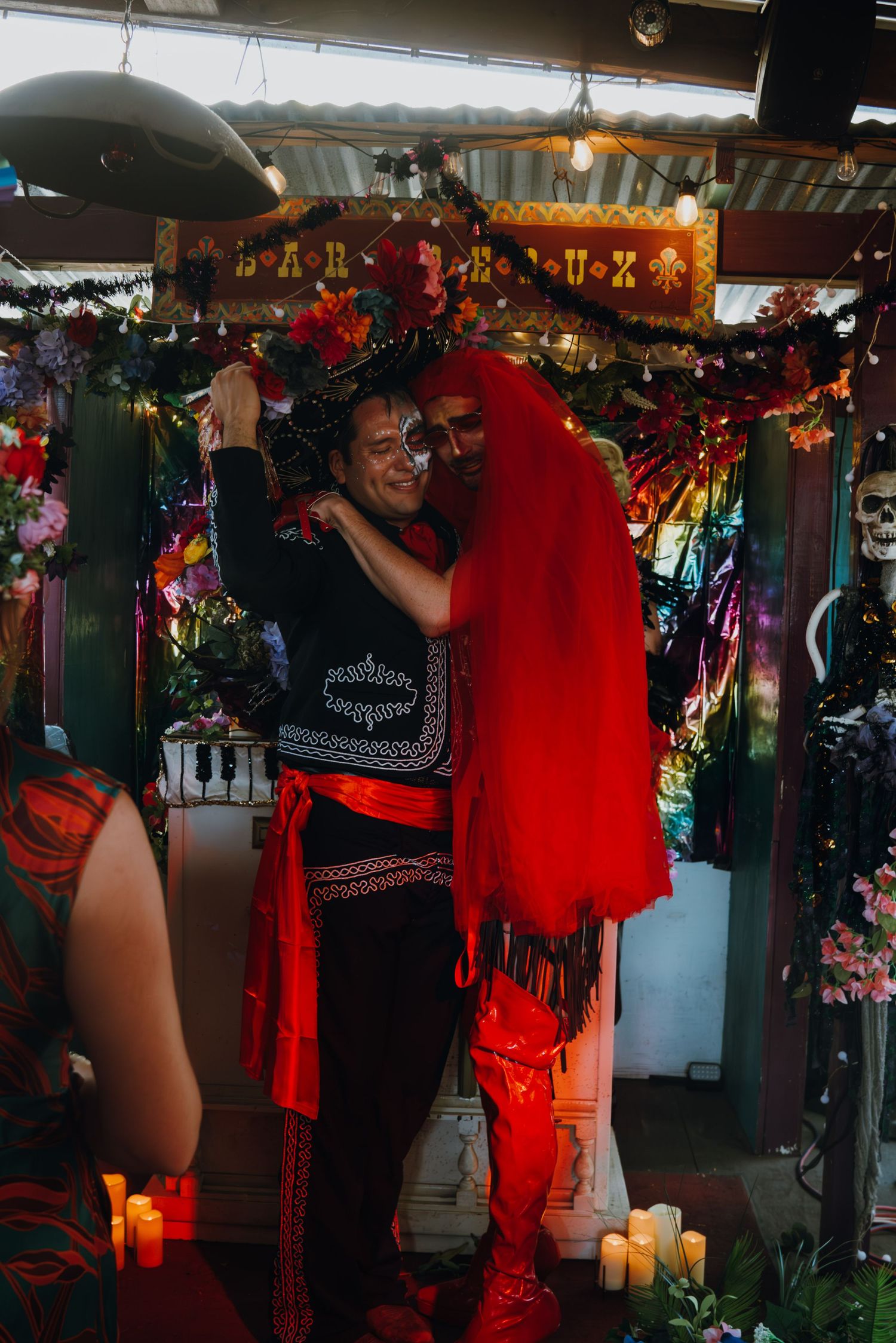 Couple embraces at a Dia de los Muertos themed wedding altar decorated with flowers and candles.