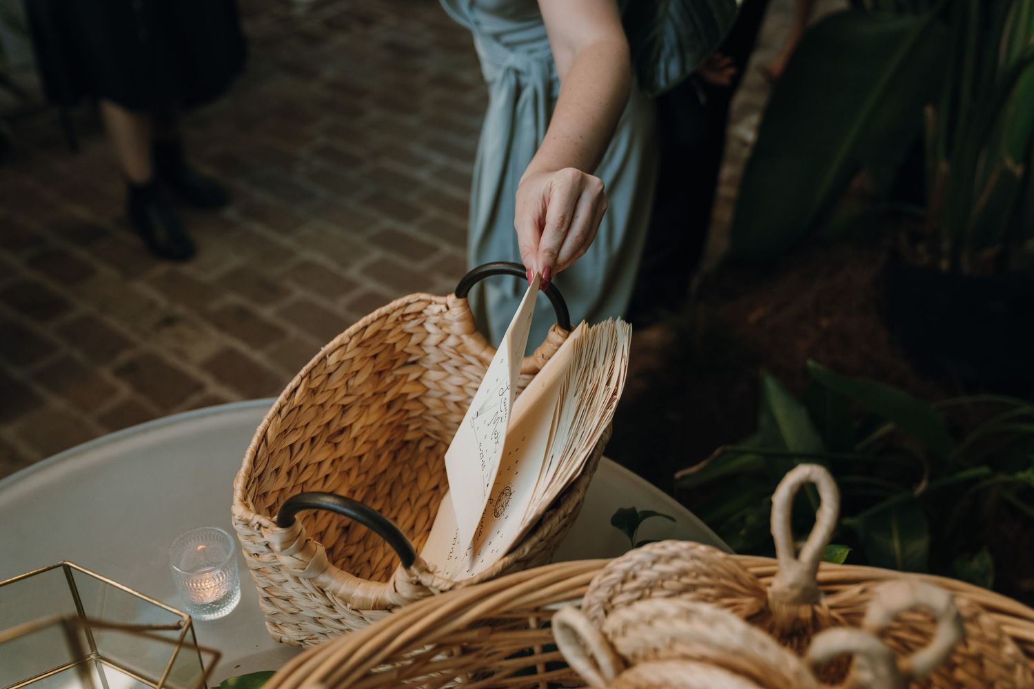 A woman places woven fan programs into a wicker basket at an outdoor wedding ceremony.