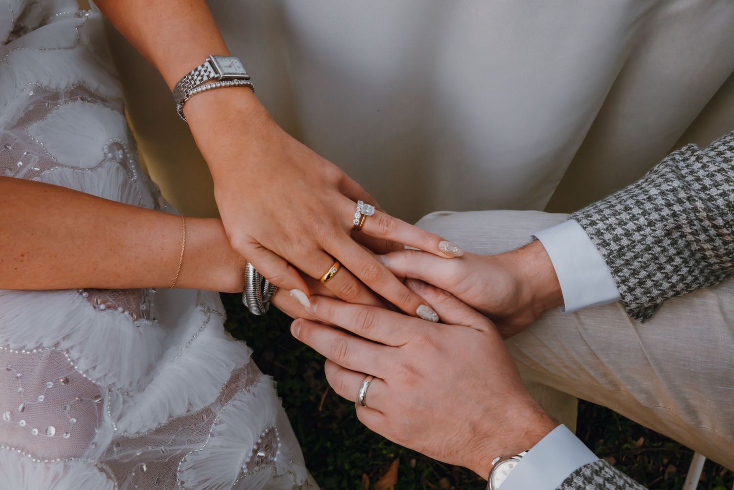 Close-up of bride and groom holding hands together showing wedding rings and elegant diamond bracelets.