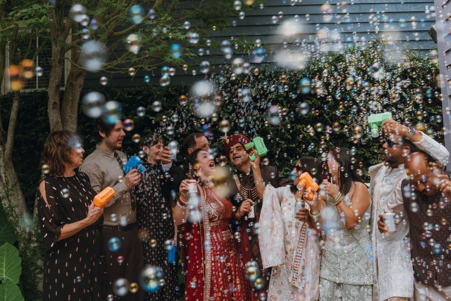 Group of guests celebrating with bubble guns at a colorful Indian wedding outdoor ceremony.