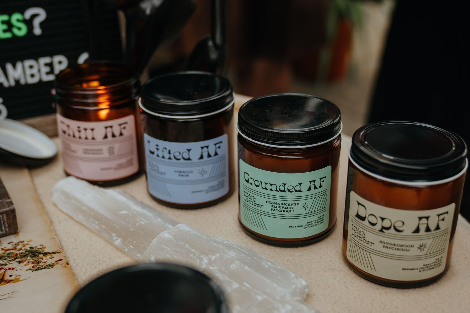 Four labeled scented candle jars in black tins arranged on a table at a market display.