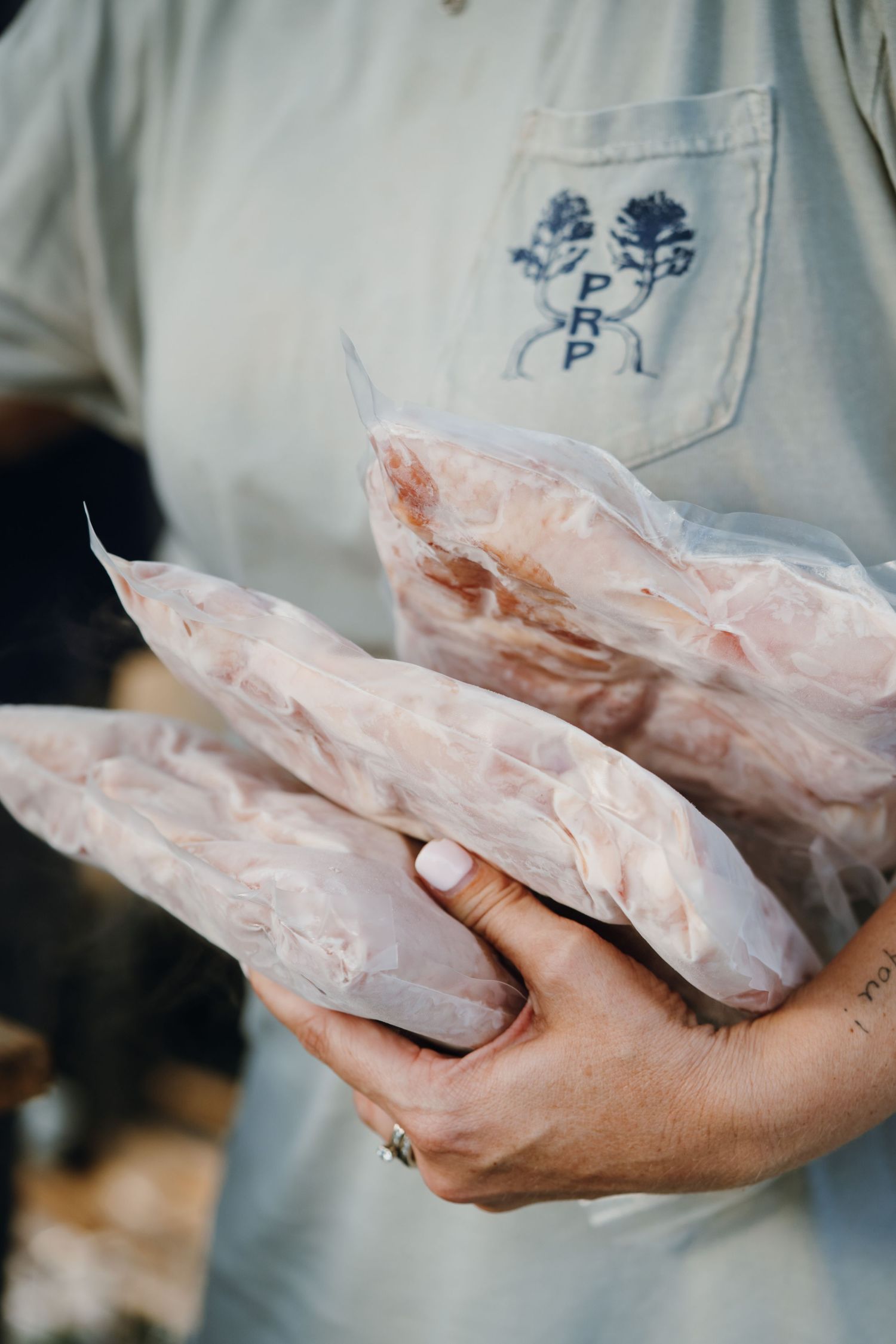 Person holding raw meat cuts wrapped in plastic at an outdoor market or butcher shop.