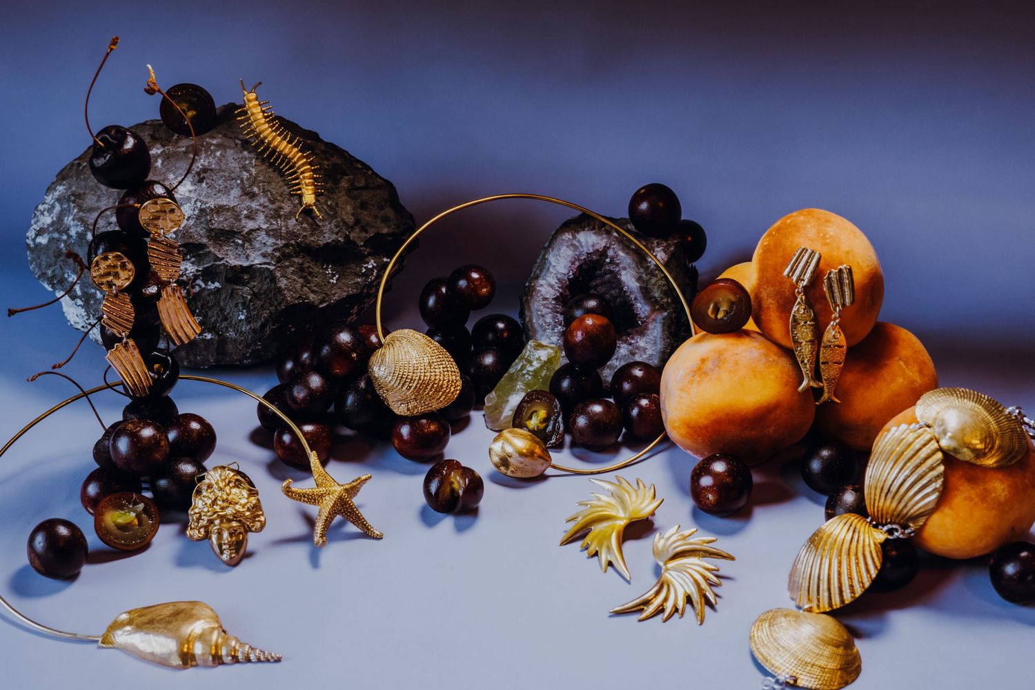 Gold jewelry collection with shells, starfish, and beads arranged with fruit and stones.