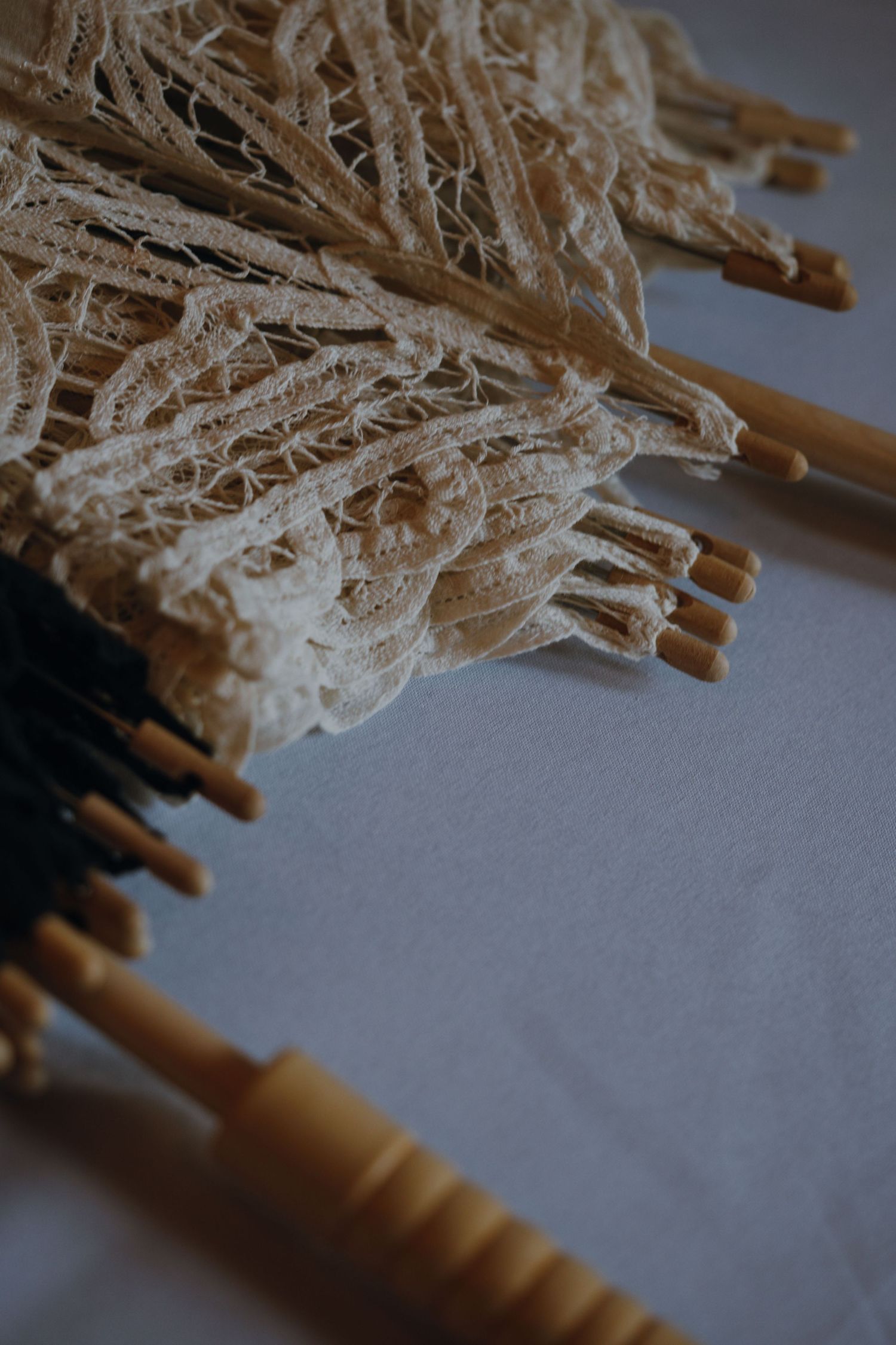 Close-up of delicate cream lace parasols with wooden handles arranged on a white surface for a wedding.