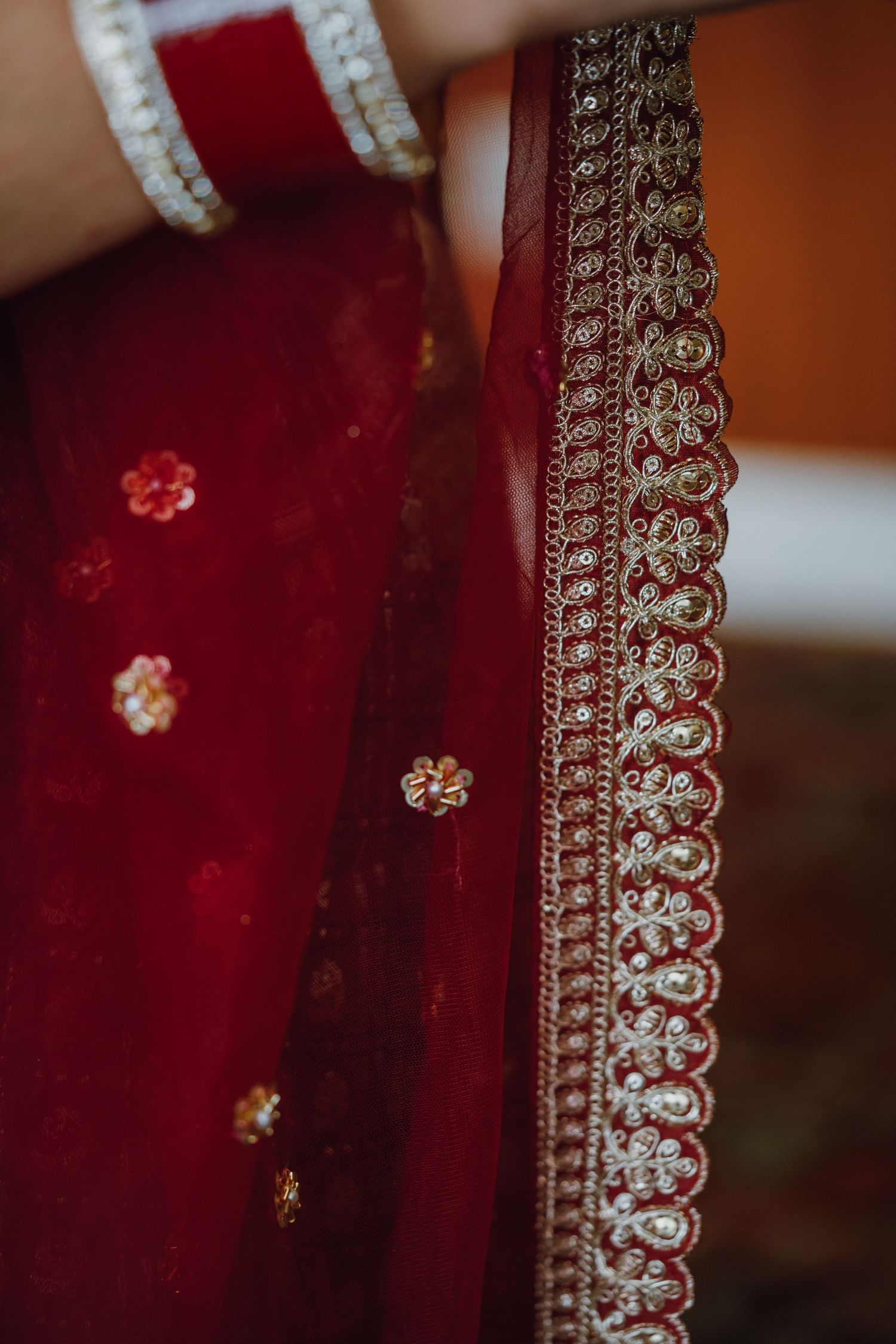 Intricate gold embroidery border detail on a deep red Indian bridal dupatta with floral embellishments.